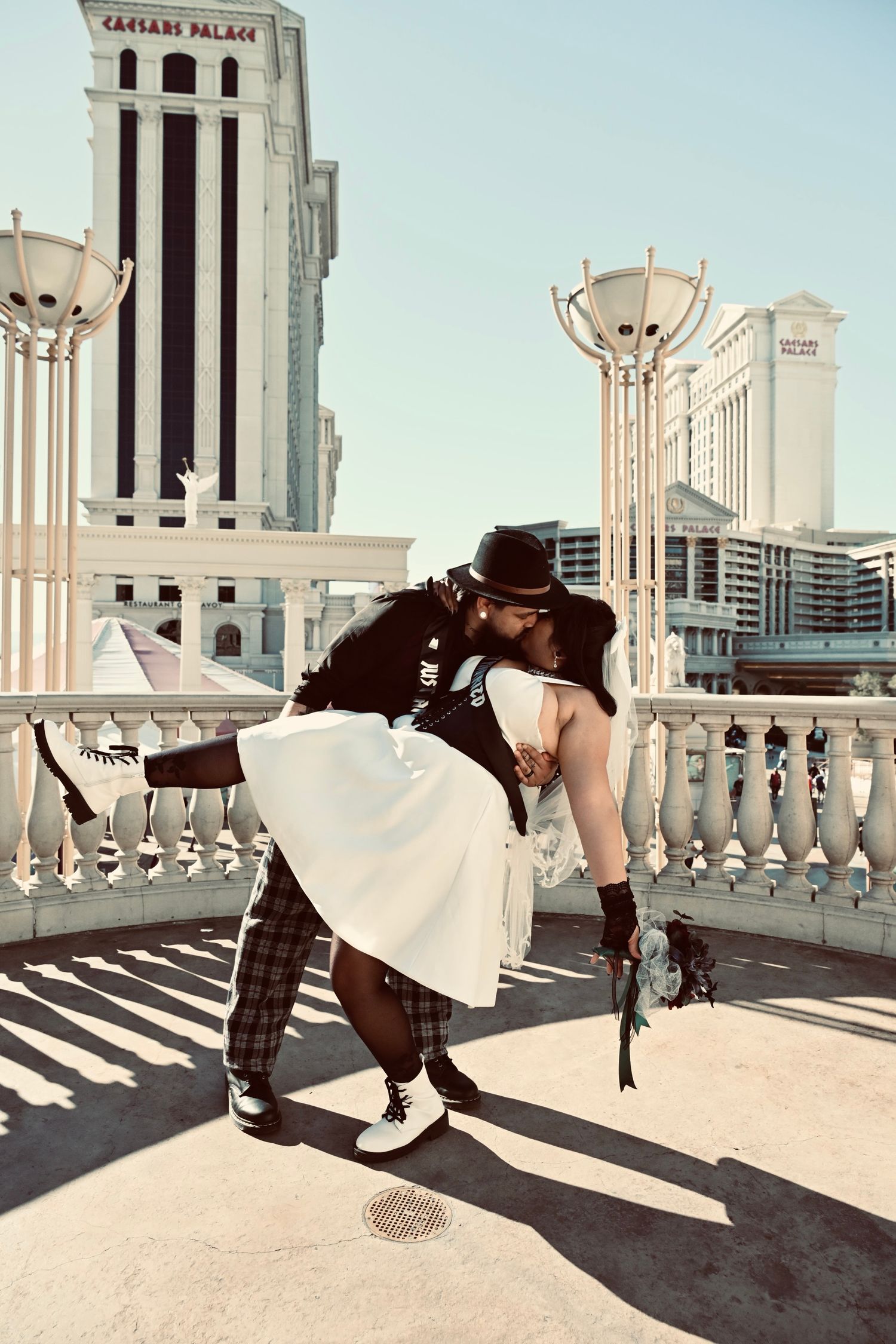 Newlywed couple sharing a romantic dip kiss on a Las Vegas strip balcony with Caesars Palace in the background.
