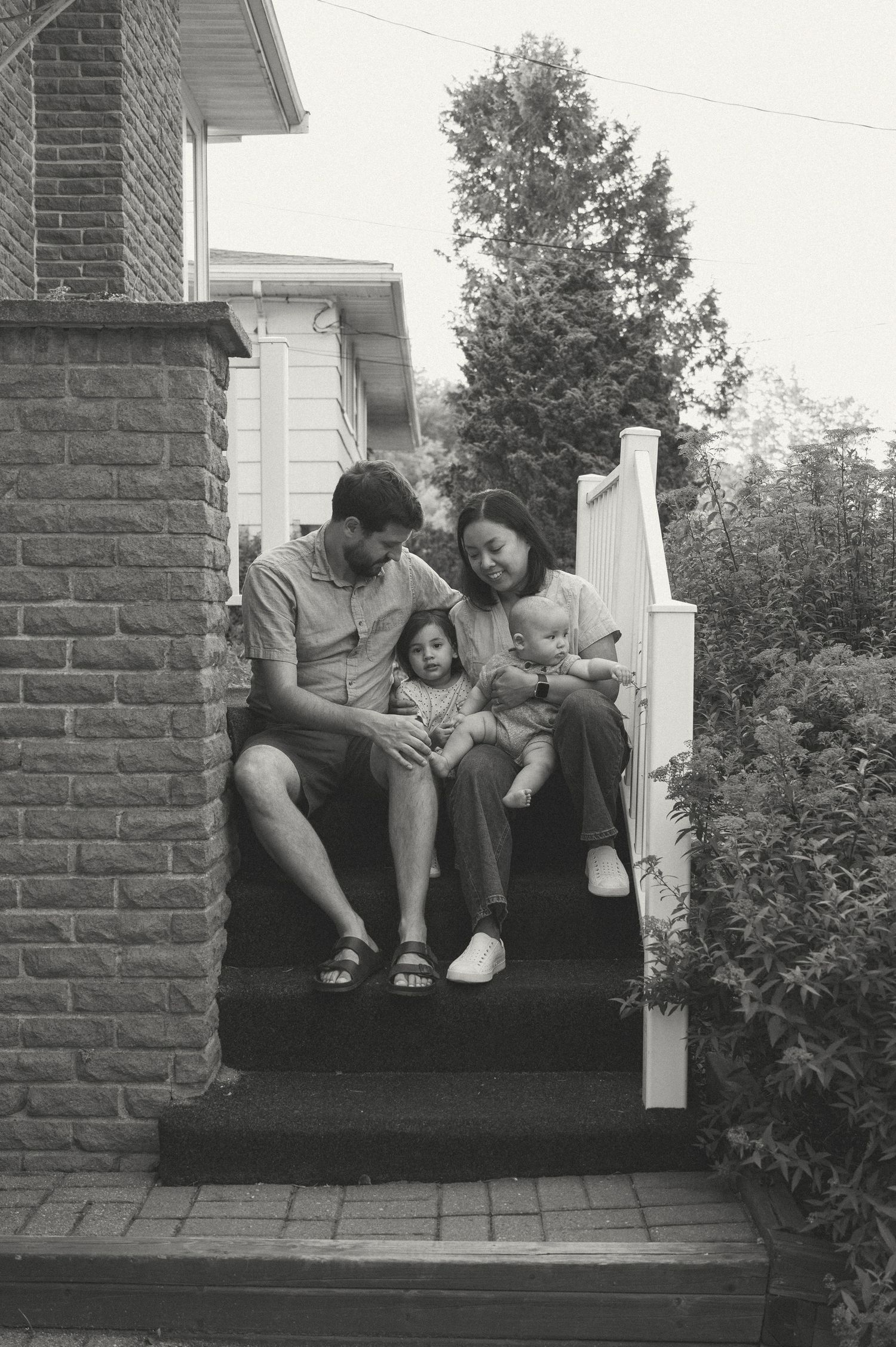 A family sits together on brick steps outside their home in a tender vintage black and white photograph.