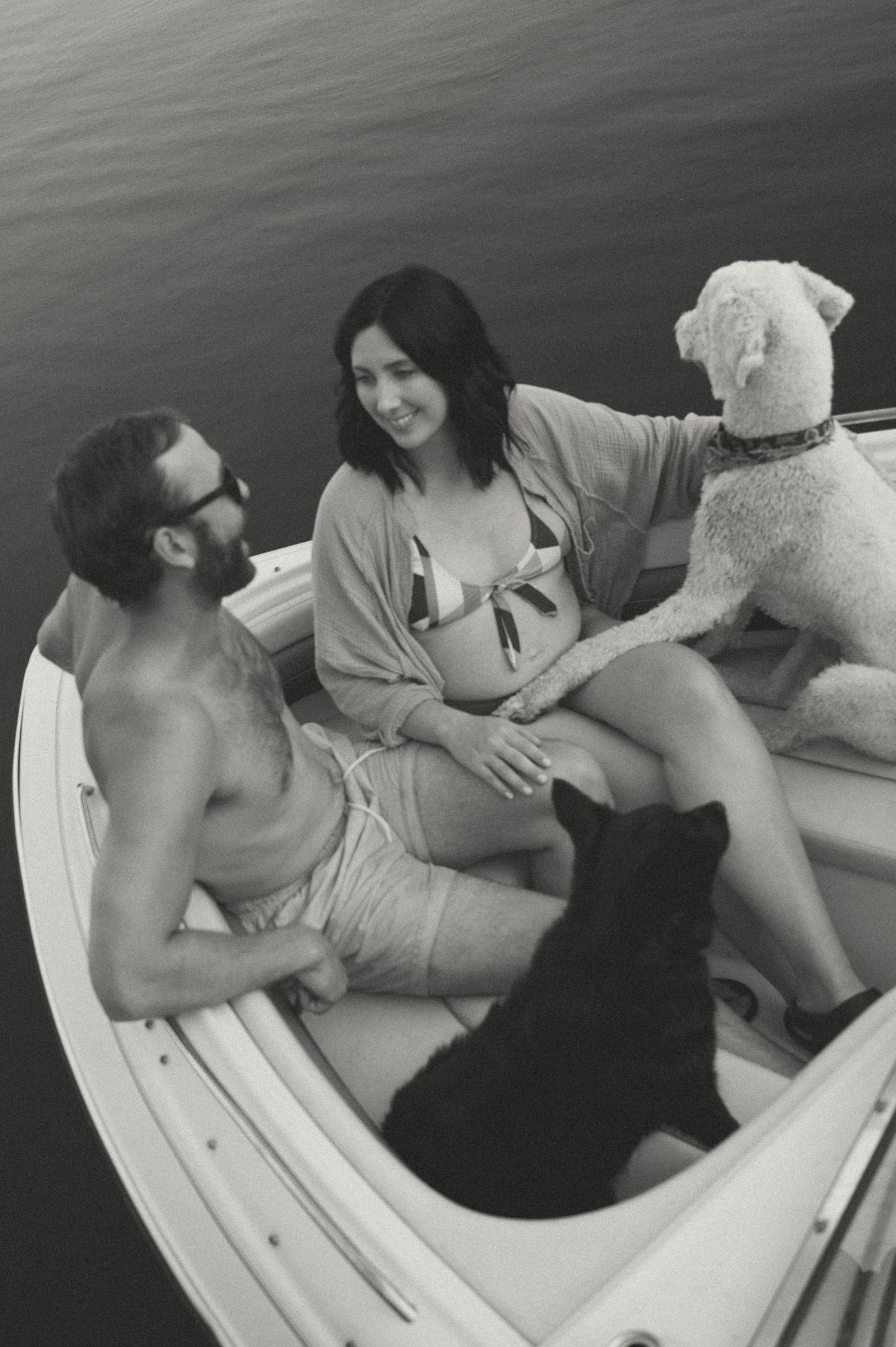 Maternity session for a relaxed couple lounging in their boat with their dogs on a calm day.
