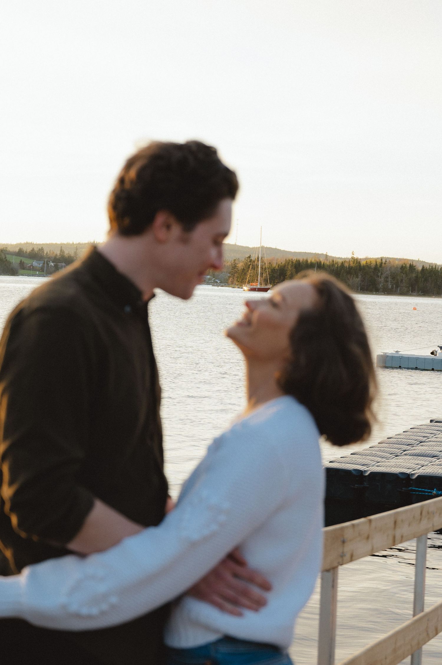 A couples photo session sharing a romantic moment by the water at sunset with boats in the background.