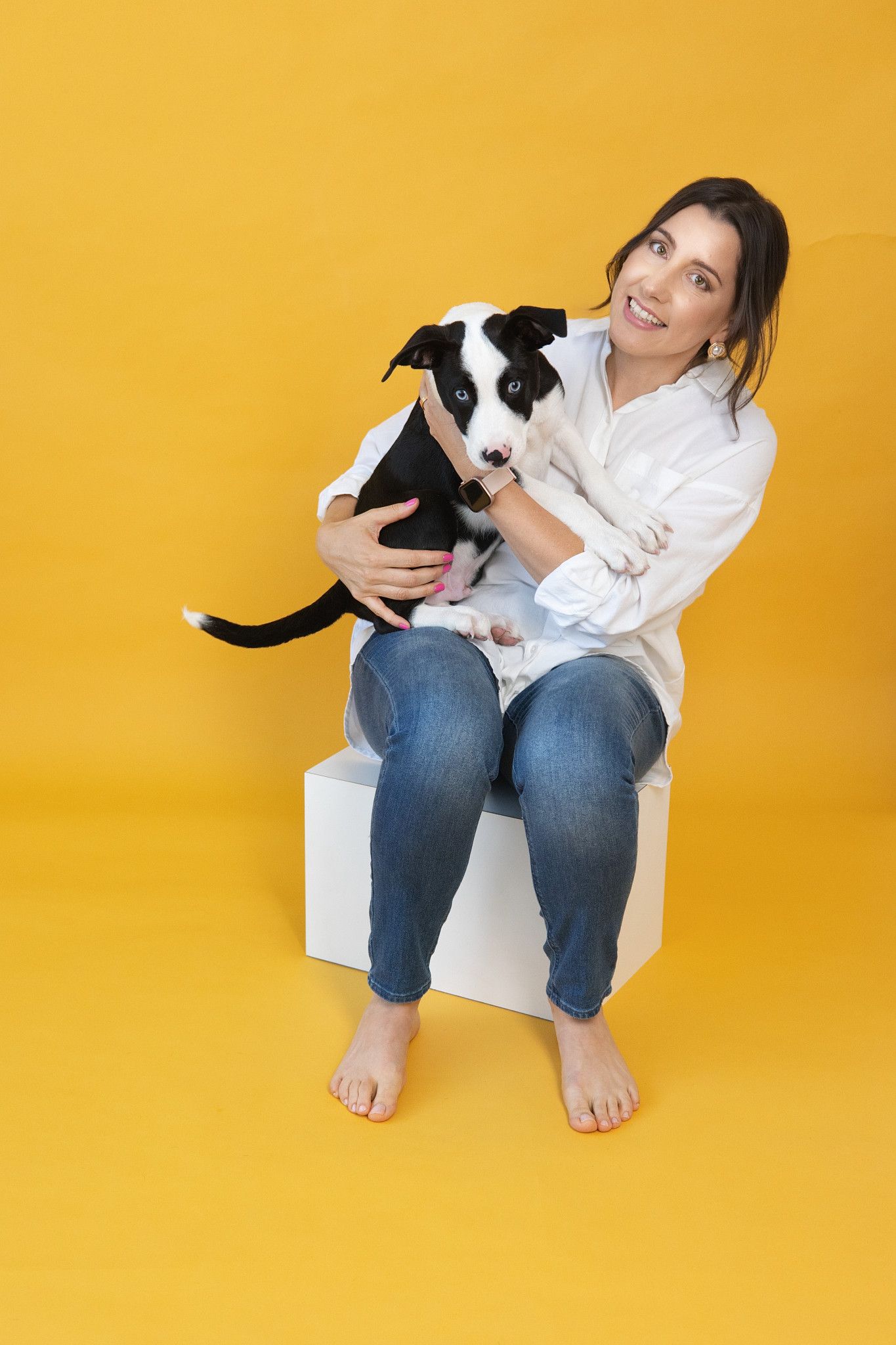 Smiling woman in white shirt holding black and white puppy on yellow background.
