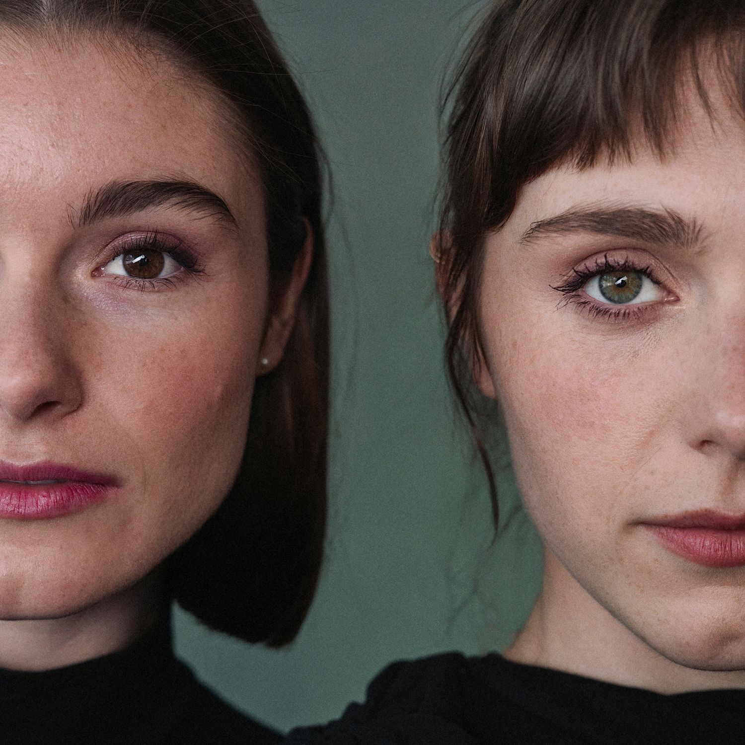 Two young women with brown hair pose closely together against a green background, wearing black tops.