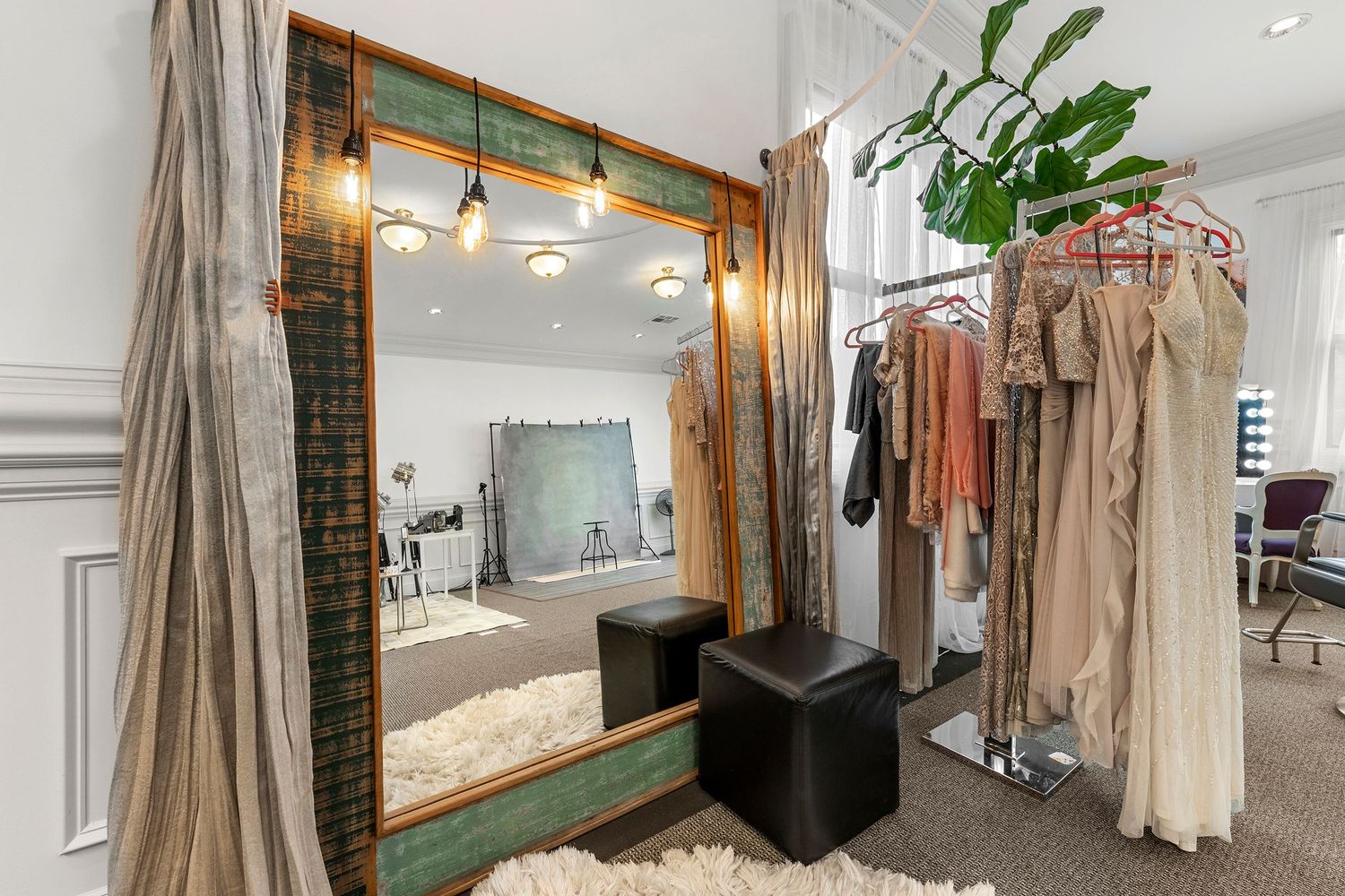 Boutique dressing room with vintage green-framed mirror, hanging garments on rack, and shag rug.