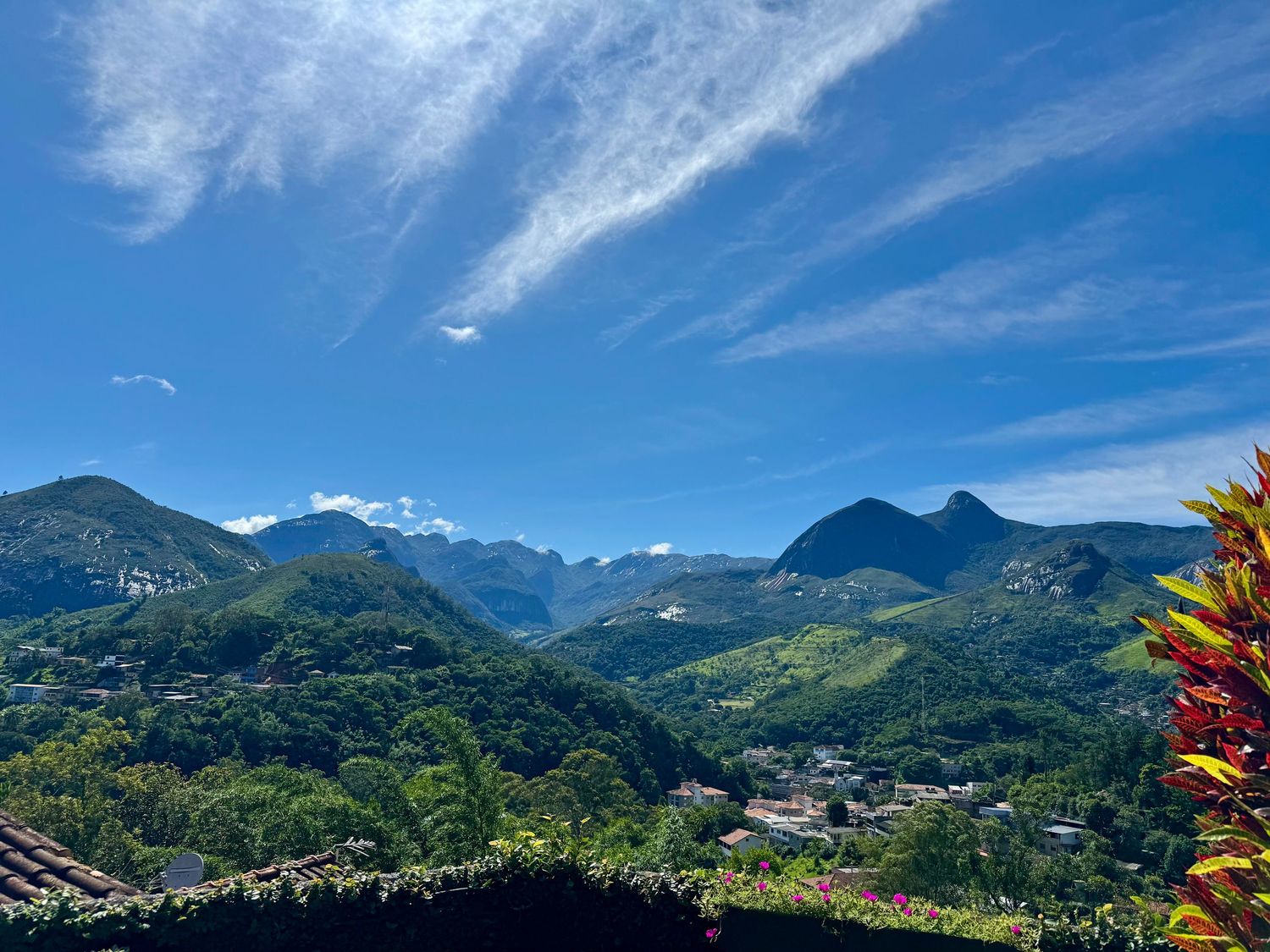 Panoramic view of lush green mountains under a vivid blue sky with wispy clouds in a tropical town setting.