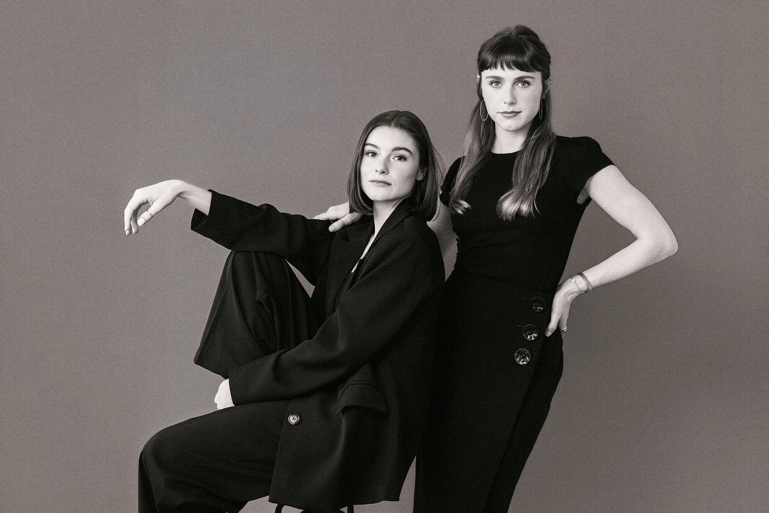 Two women in black outfits posing together in black and white portrait photo.