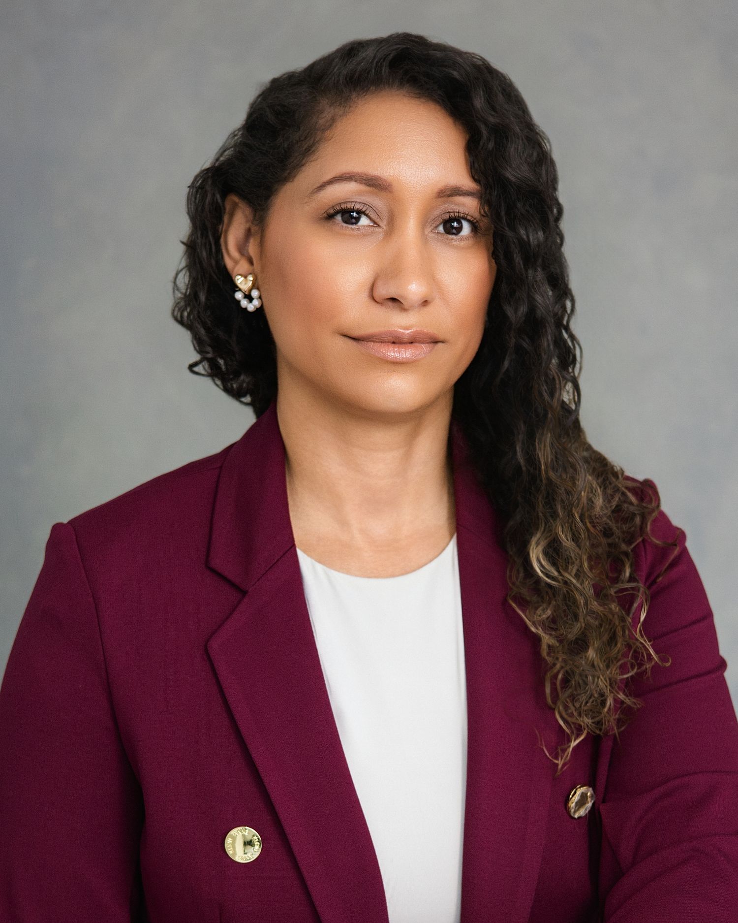 Professional woman in burgundy blazer poses for formal corporate headshot portrait.