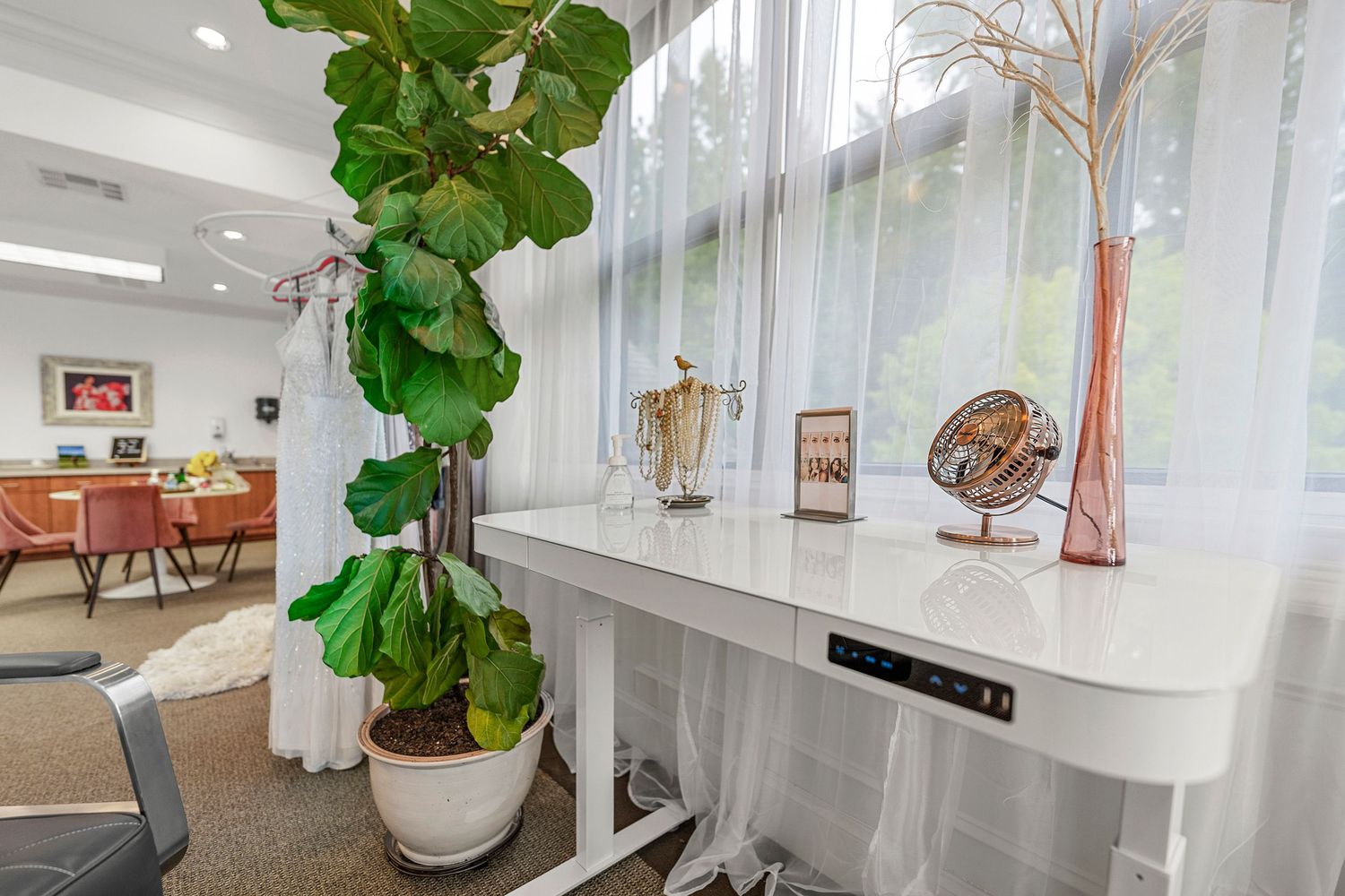 Modern white console table with decorative accessories beside sheer curtains and large tropical plant.