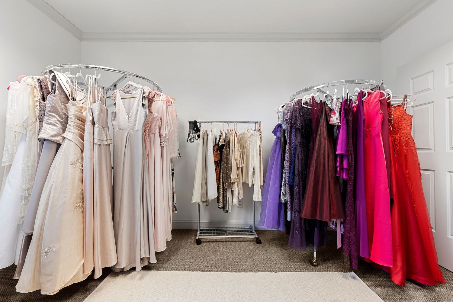 Wardrobe room with racks of colorful formal gowns ranging from white to vibrant red and pink.