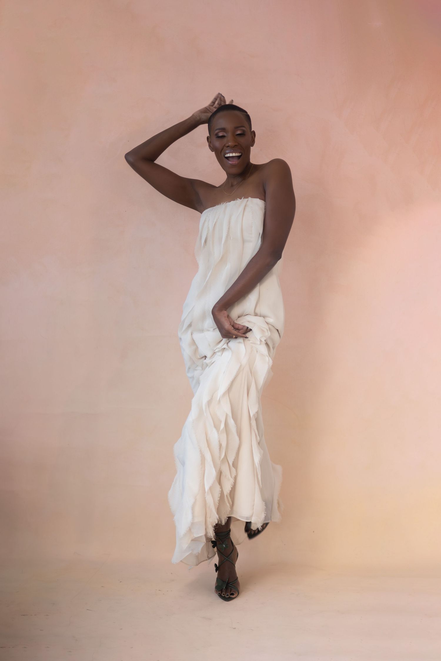 Smiling woman in flowing white dress against peach background