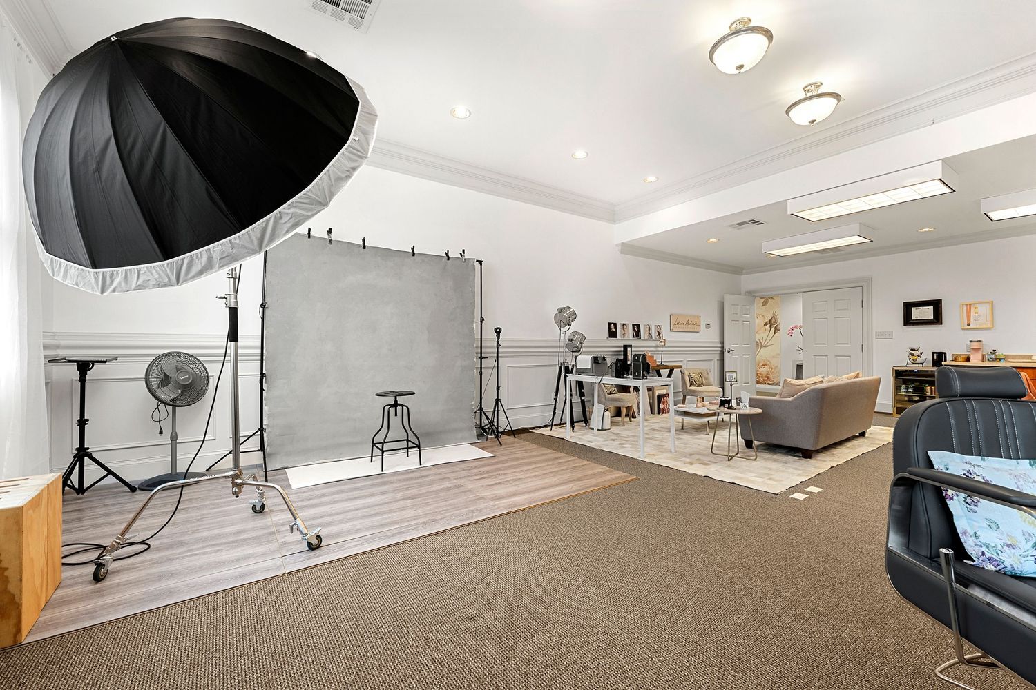 Spacious photography studio featuring large umbrella light, gray backdrop, and cozy lounge area.