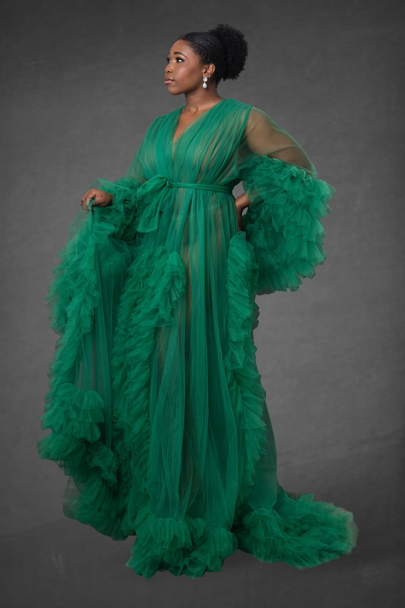 Woman in elegant emerald green ruffled tulle gown posing against gray backdrop.