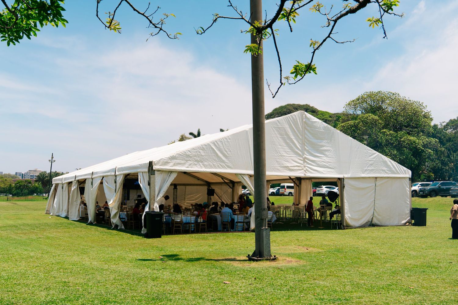 Large white event tent on green grass field with guests dining inside on a sunny day.