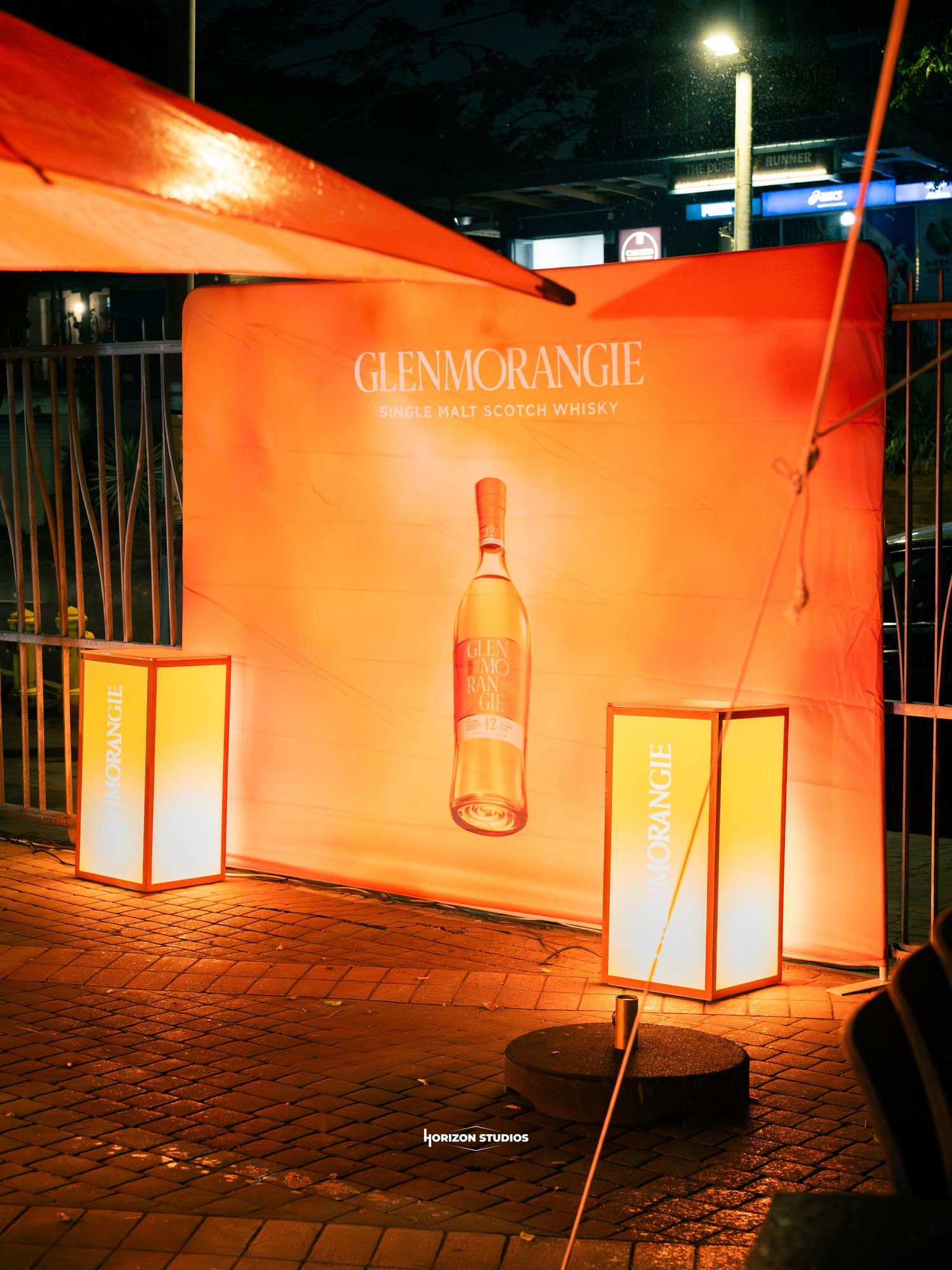 Glenmorangie Single Malt Scotch Whisky promotional display with orange backdrop and illuminated lanterns at night event.
