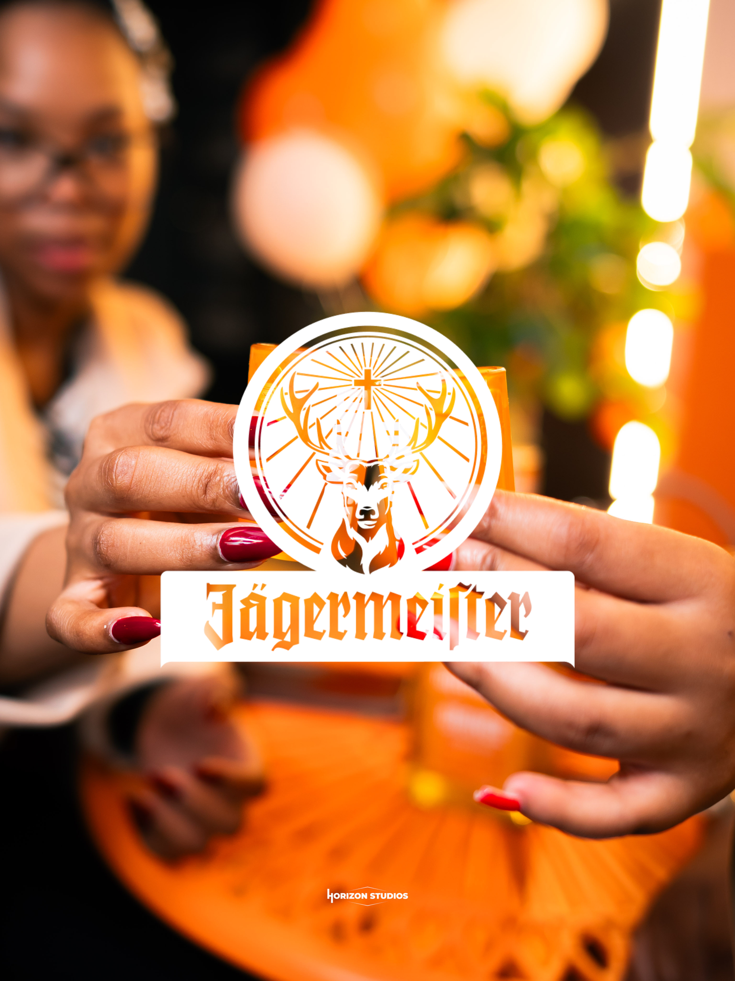 Woman holding a Jägermeister logo sticker with orange bokeh lights in the background.