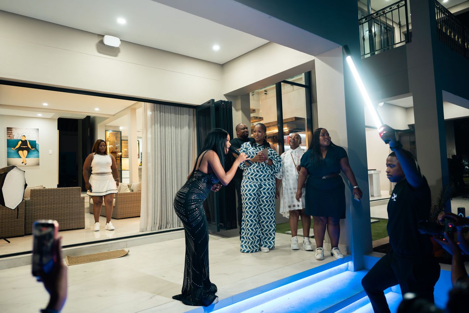 Elegant guests socializing at a luxurious evening party outside a modern home with blue LED lighting.