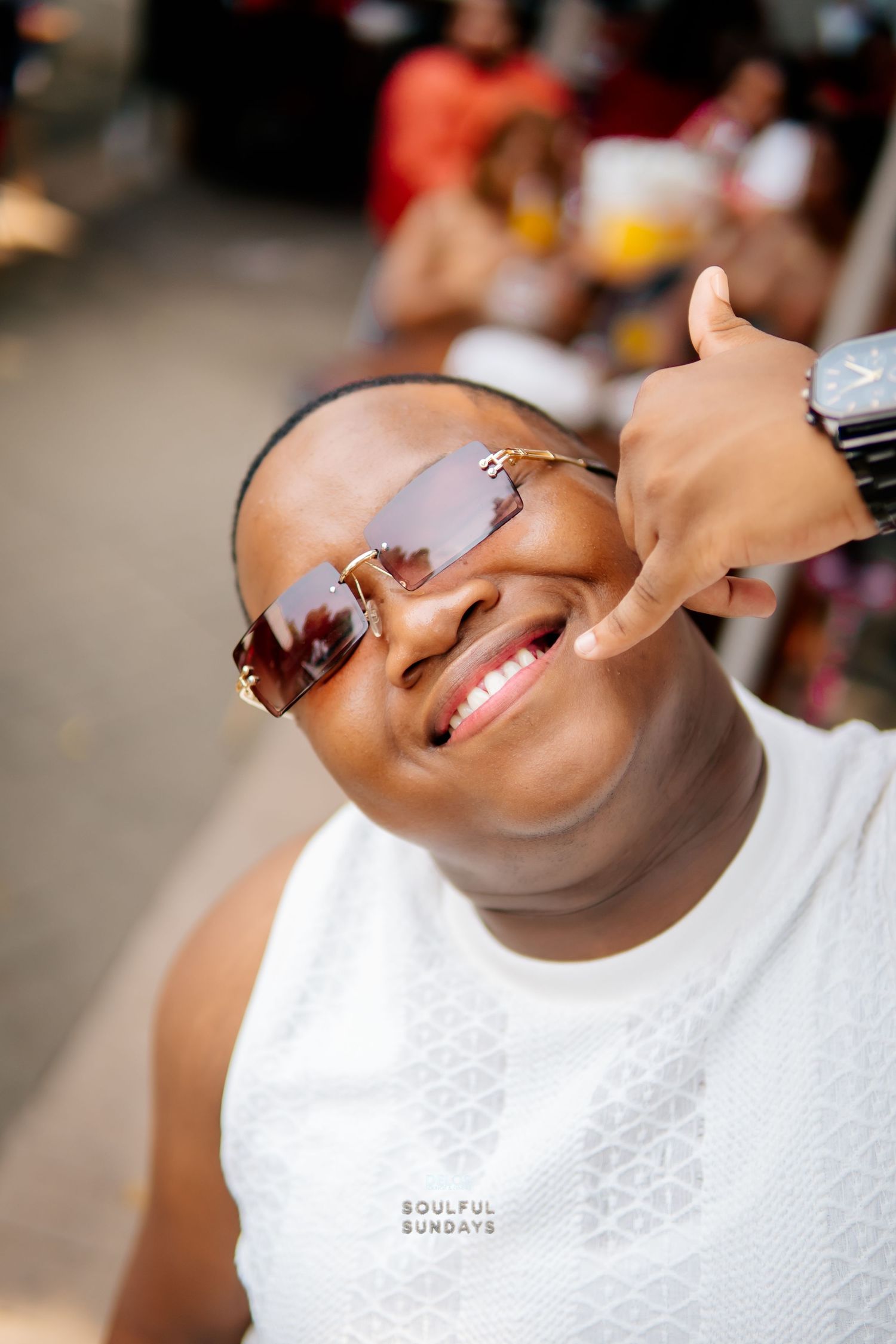 Person in white top and brown sunglasses smiling, making a peace sign gesture at a Soulful Sundays event.