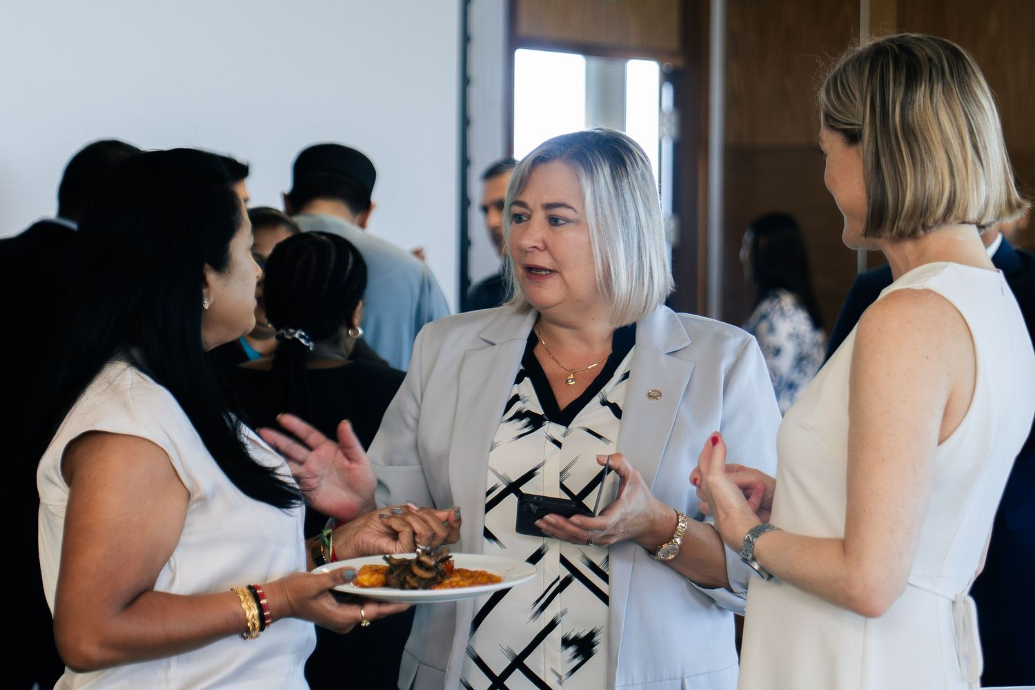 Three women engaged in conversation at a professional networking event.