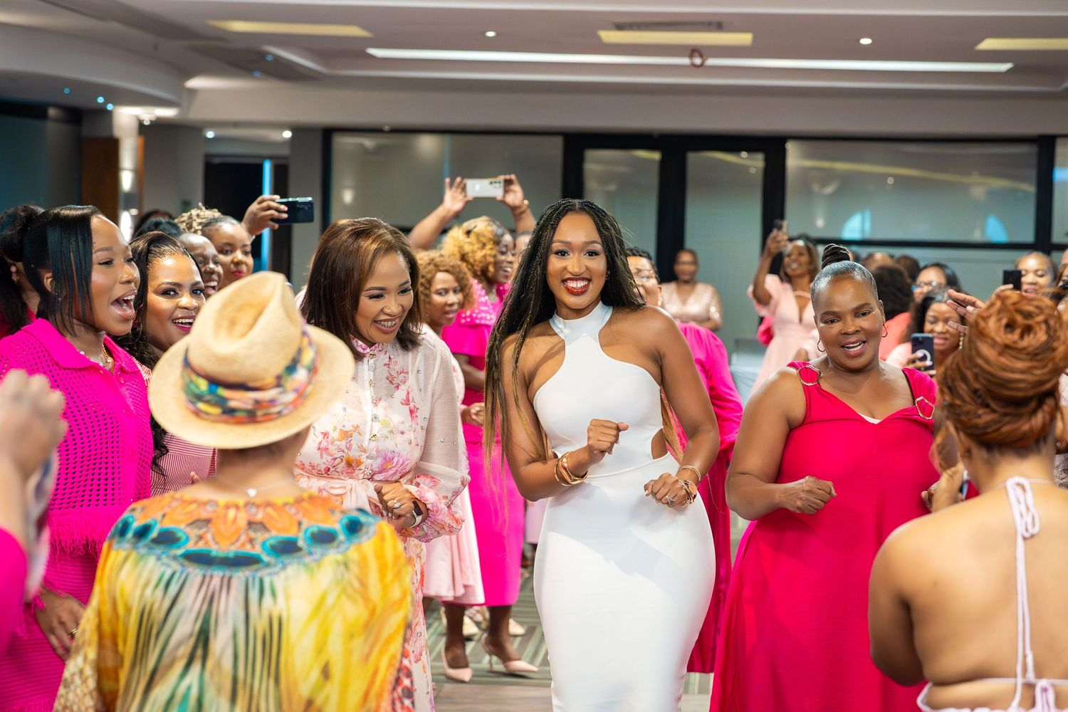Women in vibrant pink and white outfits celebrate together at a festive indoor party event.