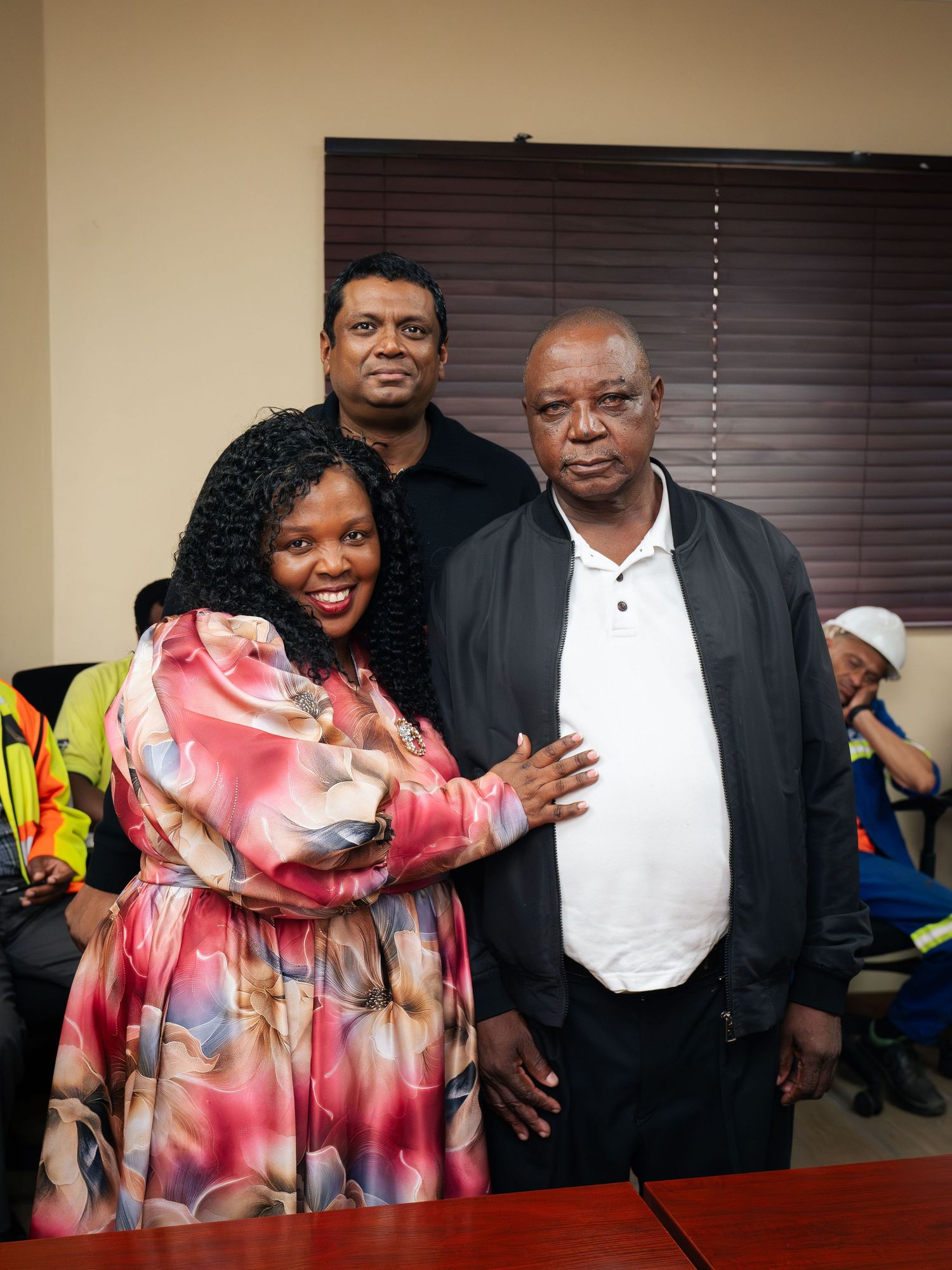 Three people posing together indoors, smiling for a photo in a professional office setting.