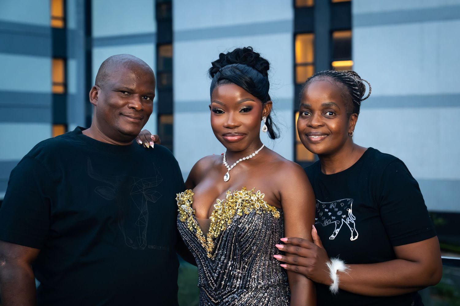 Three people posing together at an evening event, center person wearing a gold and black sequined dress.