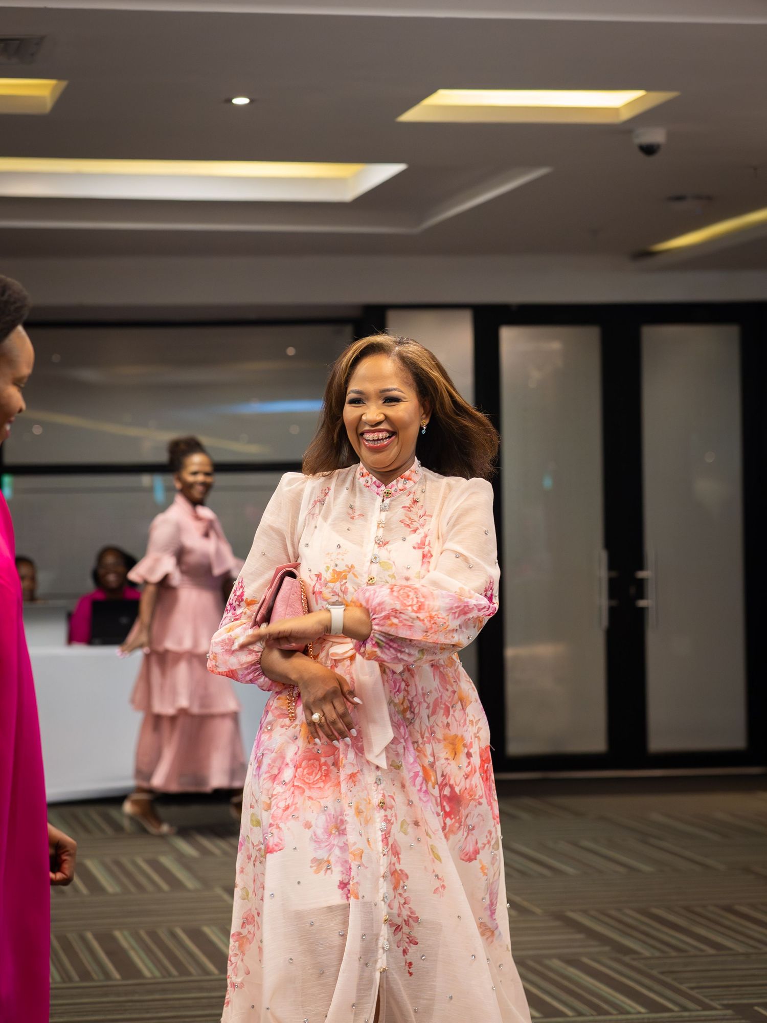 Woman smiling in floral pink dress at formal event in modern venue.