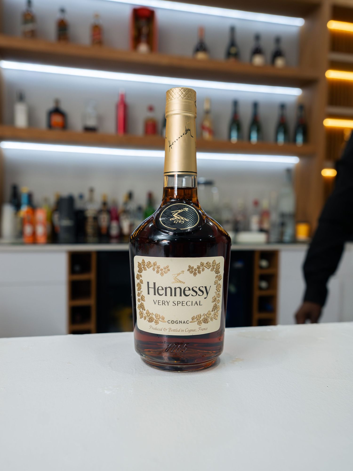 Bottle of Hennessy Very Special Cognac displayed on a white bar counter with backlit shelves behind.