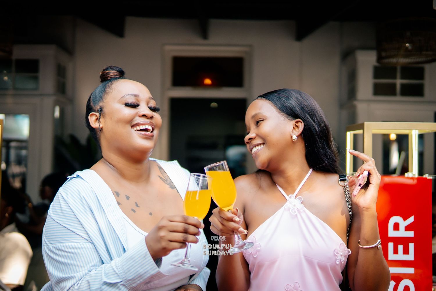 Two women smiling and toasting with champagne glasses at a brunch event, enjoying a celebratory moment together.