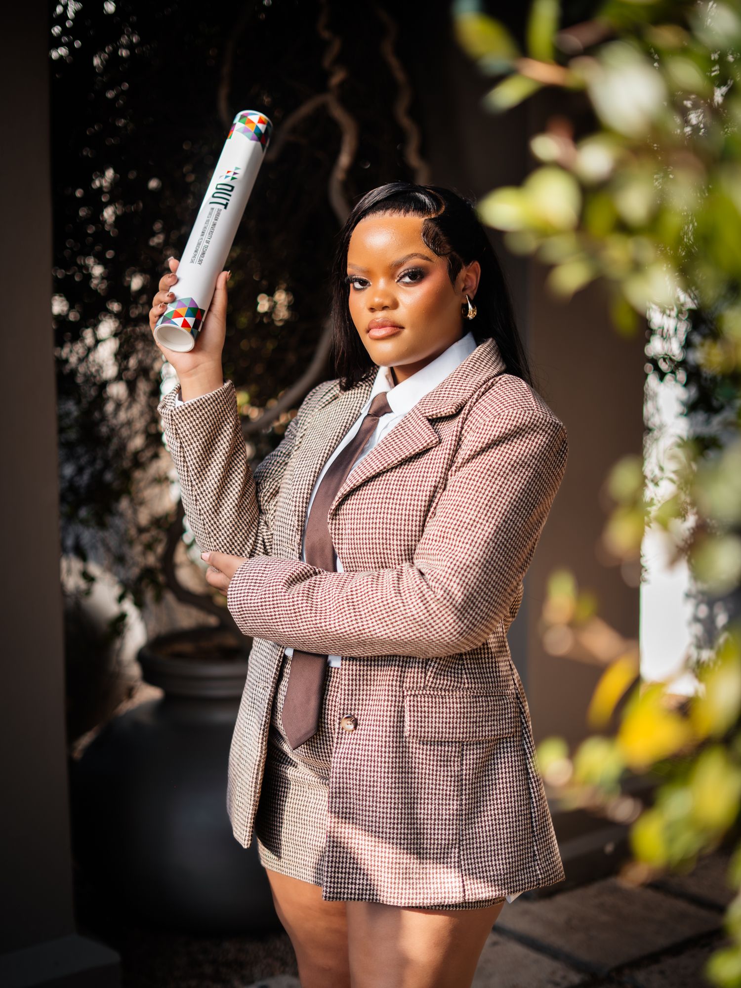 Young woman in plaid blazer and skirt set holding a hair product spray can outdoors.