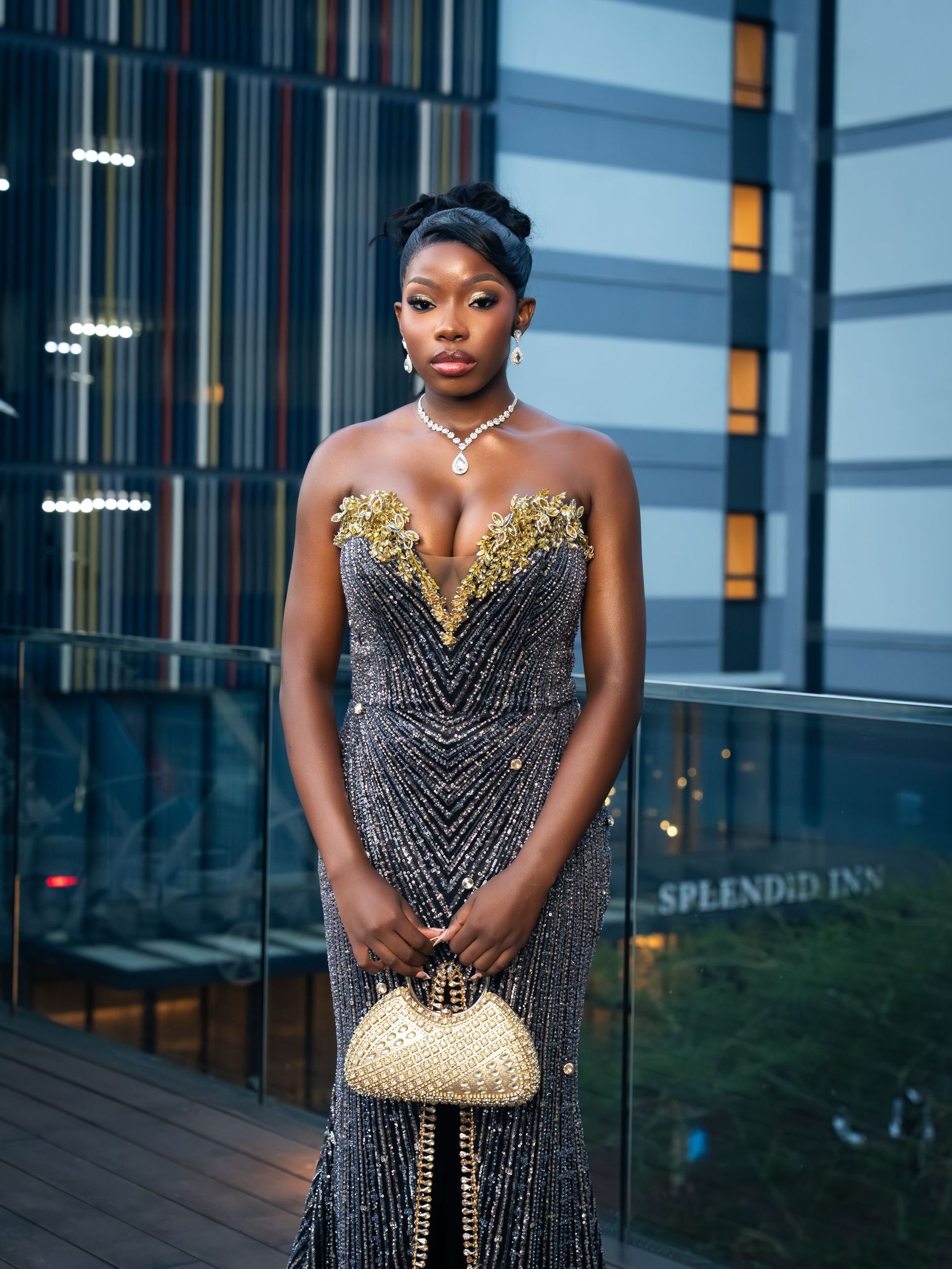 Woman in black and gold beaded strapless gown holding gold clutch, wearing diamond necklace outside Splendid Inn.