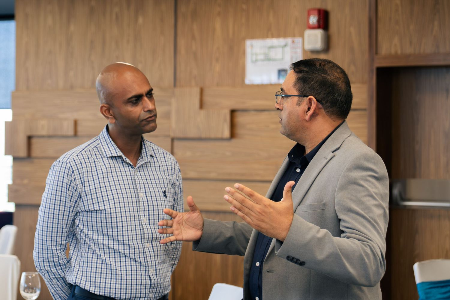 Two businessmen engaged in conversation at a modern office networking event, one gesturing expressively.