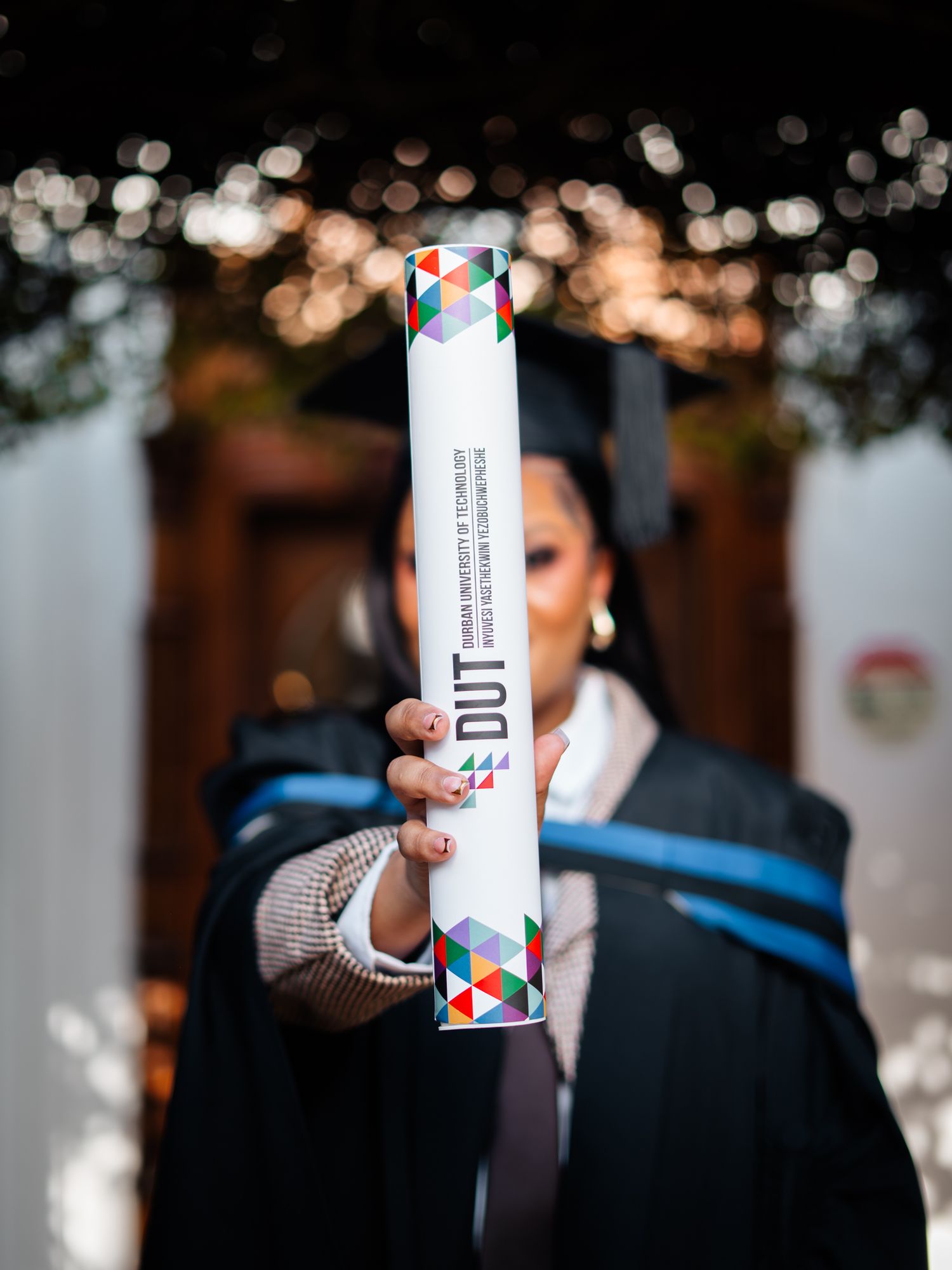 Graduate in cap and gown proudly holds DUT Durban University of Technology diploma scroll toward camera.