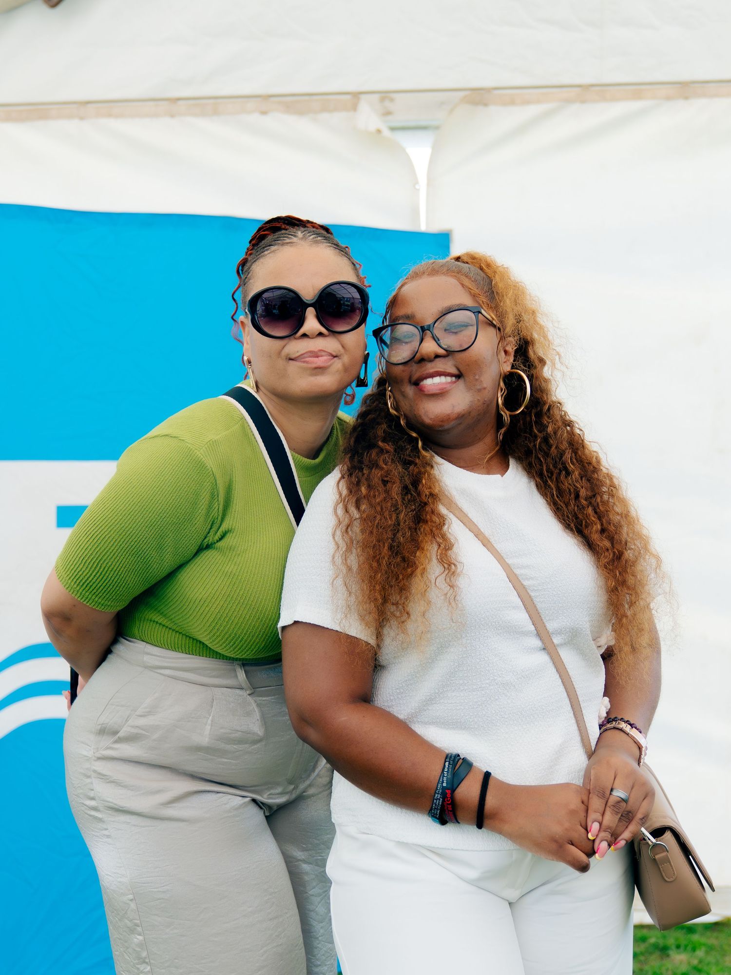 Two women smiling and posing together outdoors at an event, one in green top and one in white outfit.