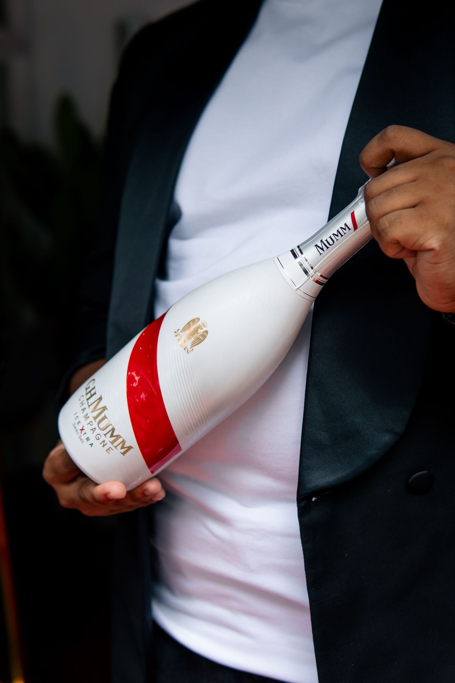 Man in black blazer holding a G.H. Mumm white and red champagne bottle at an elegant event.