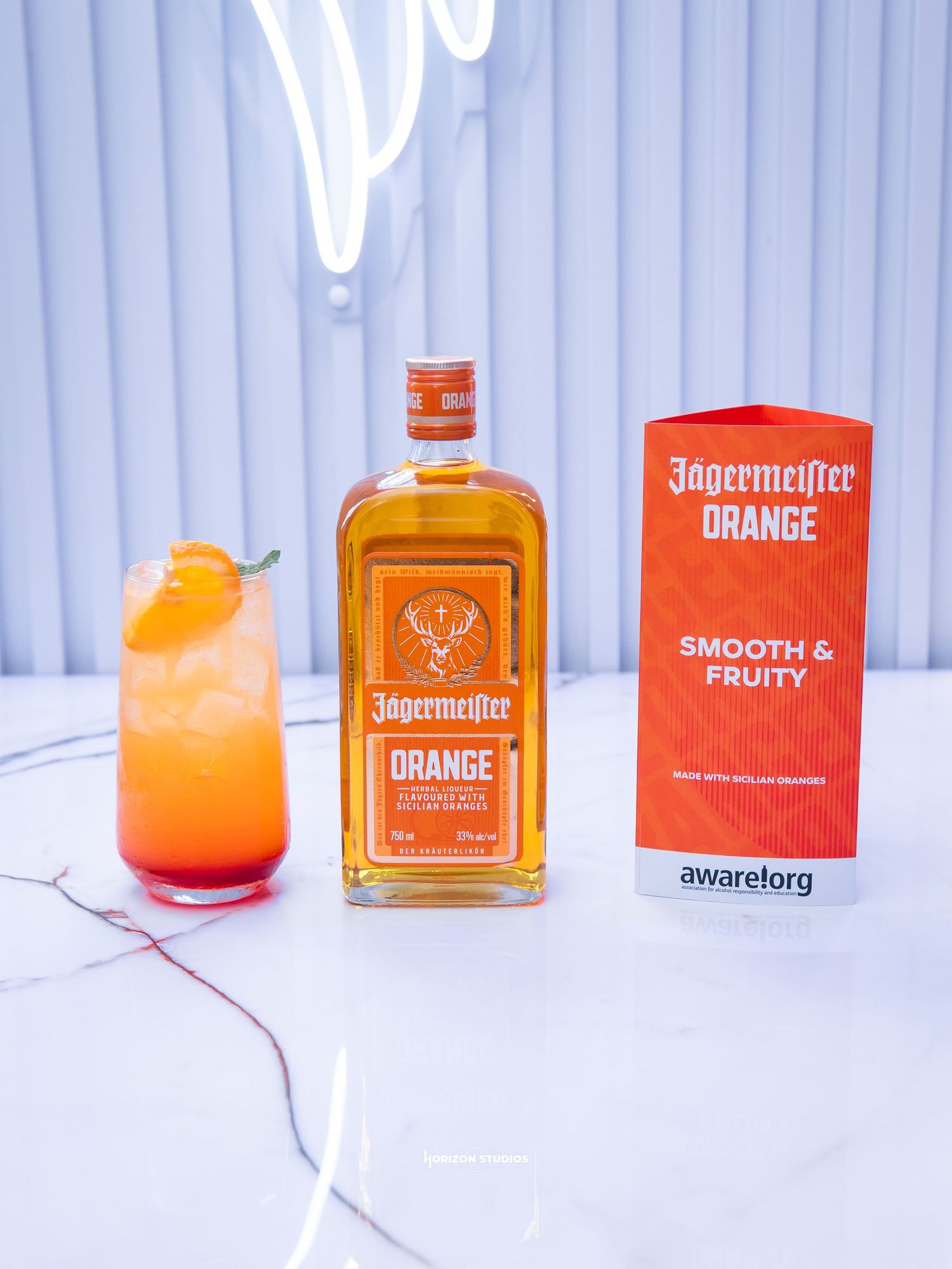 Jagermeister Orange bottle with a fruity cocktail garnished with orange peel on a marble surface.