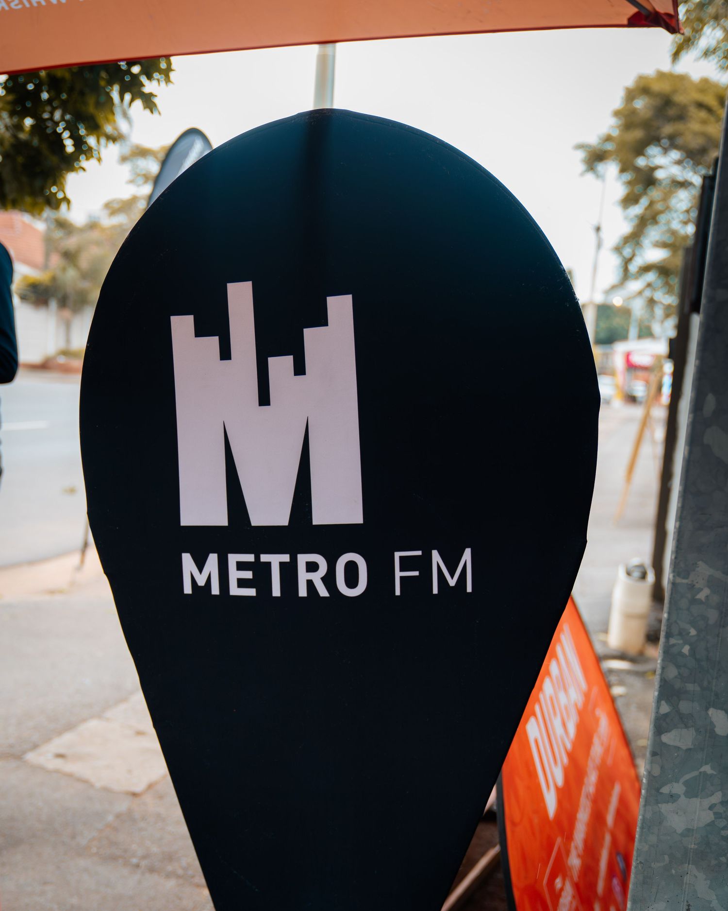 Metro FM branded teardrop banner sign displayed outdoors on a sunny street sidewalk.