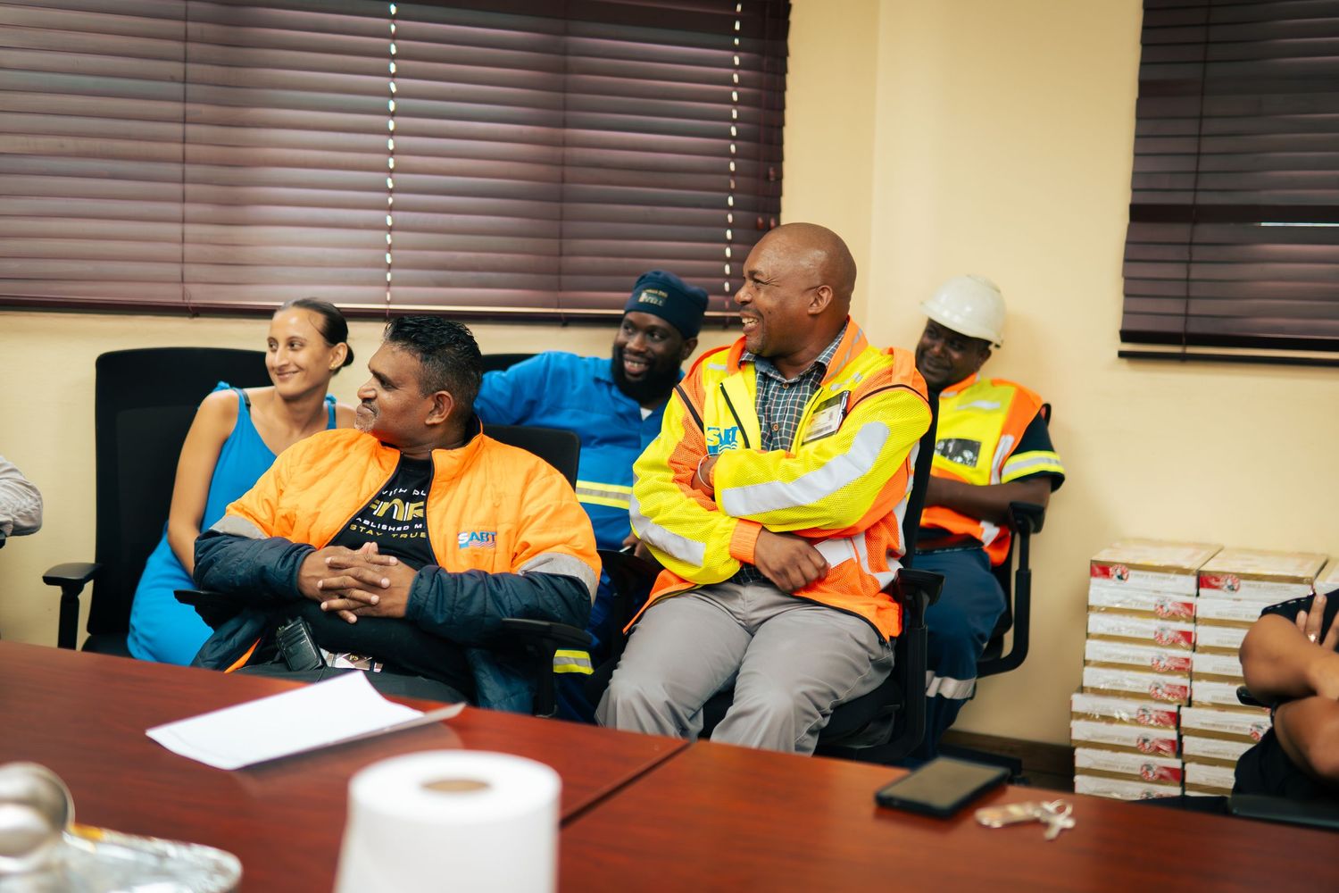 Group of workers in safety vests sitting together at a conference table during a workplace meeting.