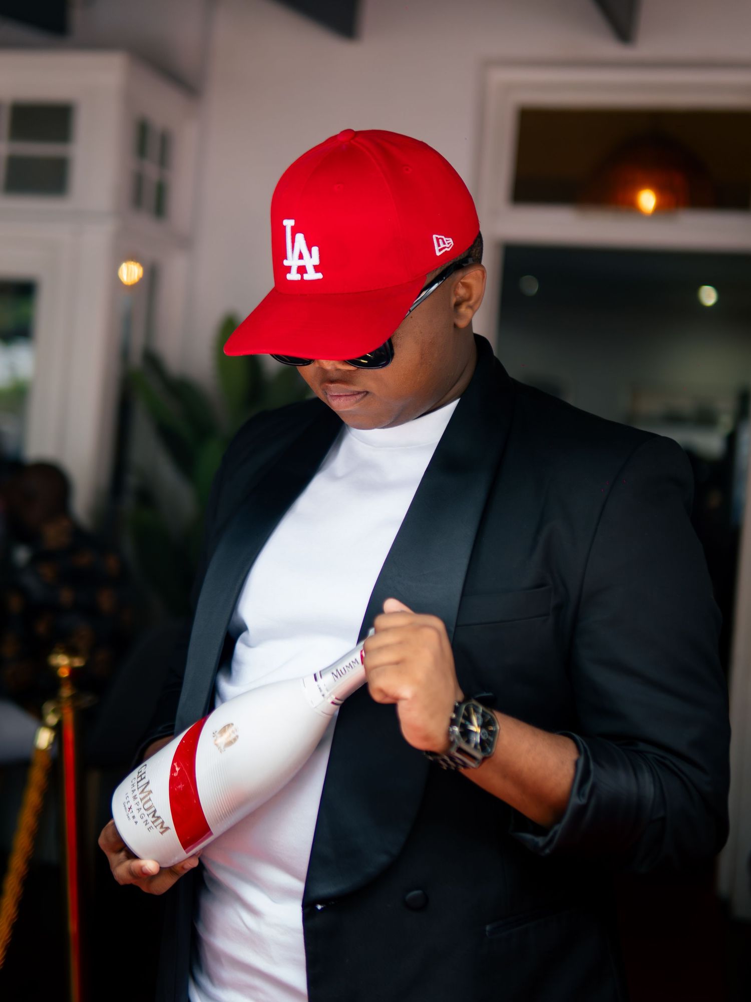 Man in red LA cap and black blazer holding a Moet champagne bottle at an upscale event.