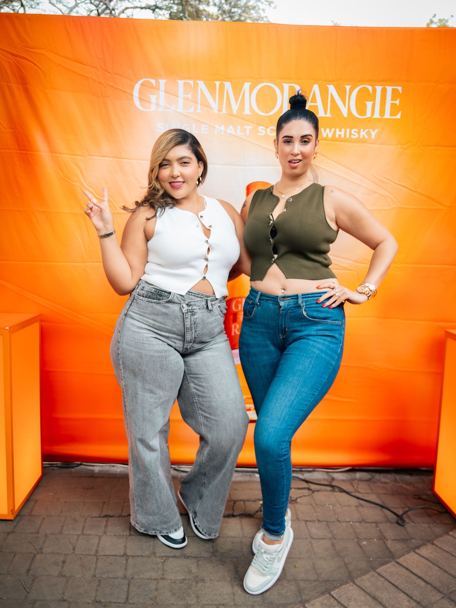 Two women posing in front of a Glenmorangie Single Malt Scotch Whisky orange backdrop at an event.