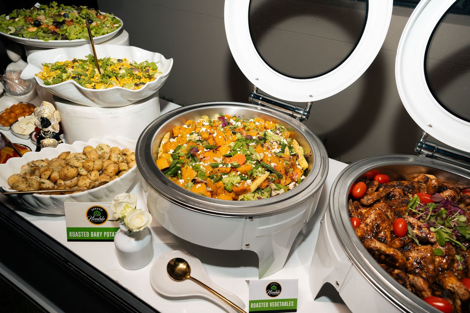A buffet spread featuring chafing dishes with colorful rice, roasted vegetables, and sauced dishes under bright circular lights.