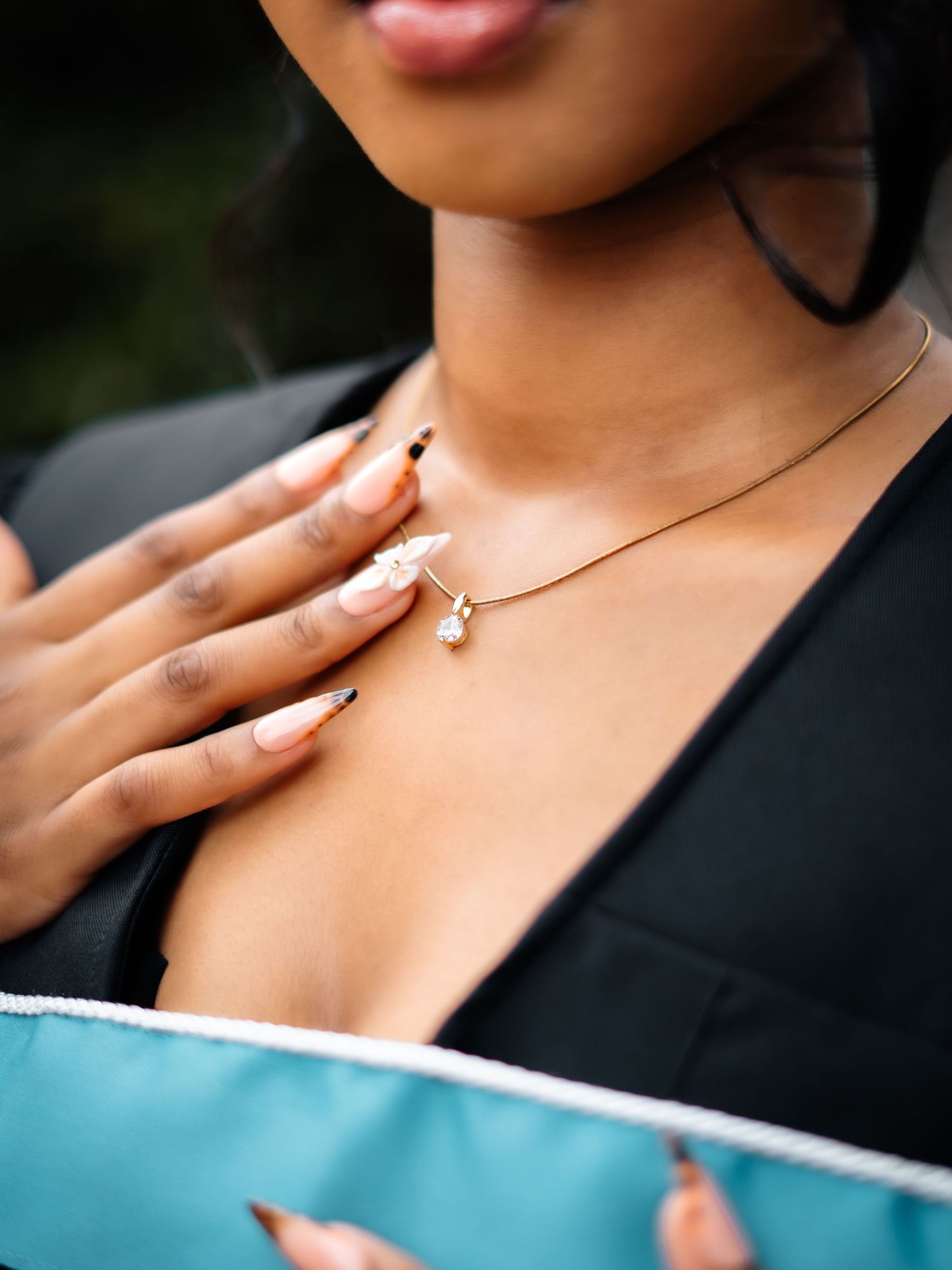 Woman wearing a gold snake chain necklace with crystal pendant, styled with black blazer and teal outfit.