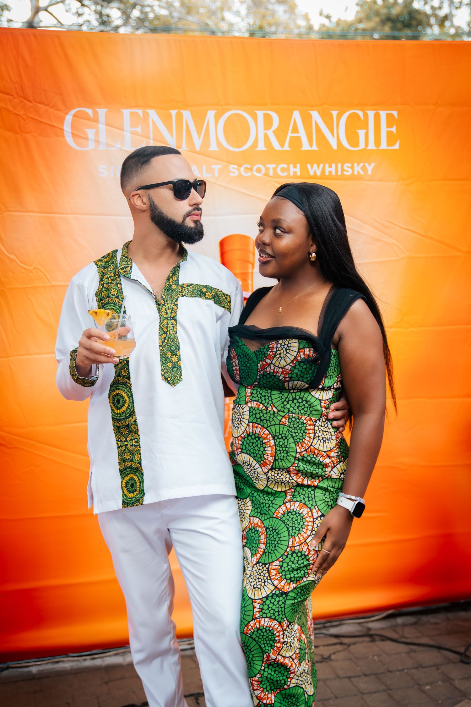 Couple in African print outfits posing at a Glenmorangie Single Malt Scotch Whisky event backdrop.
