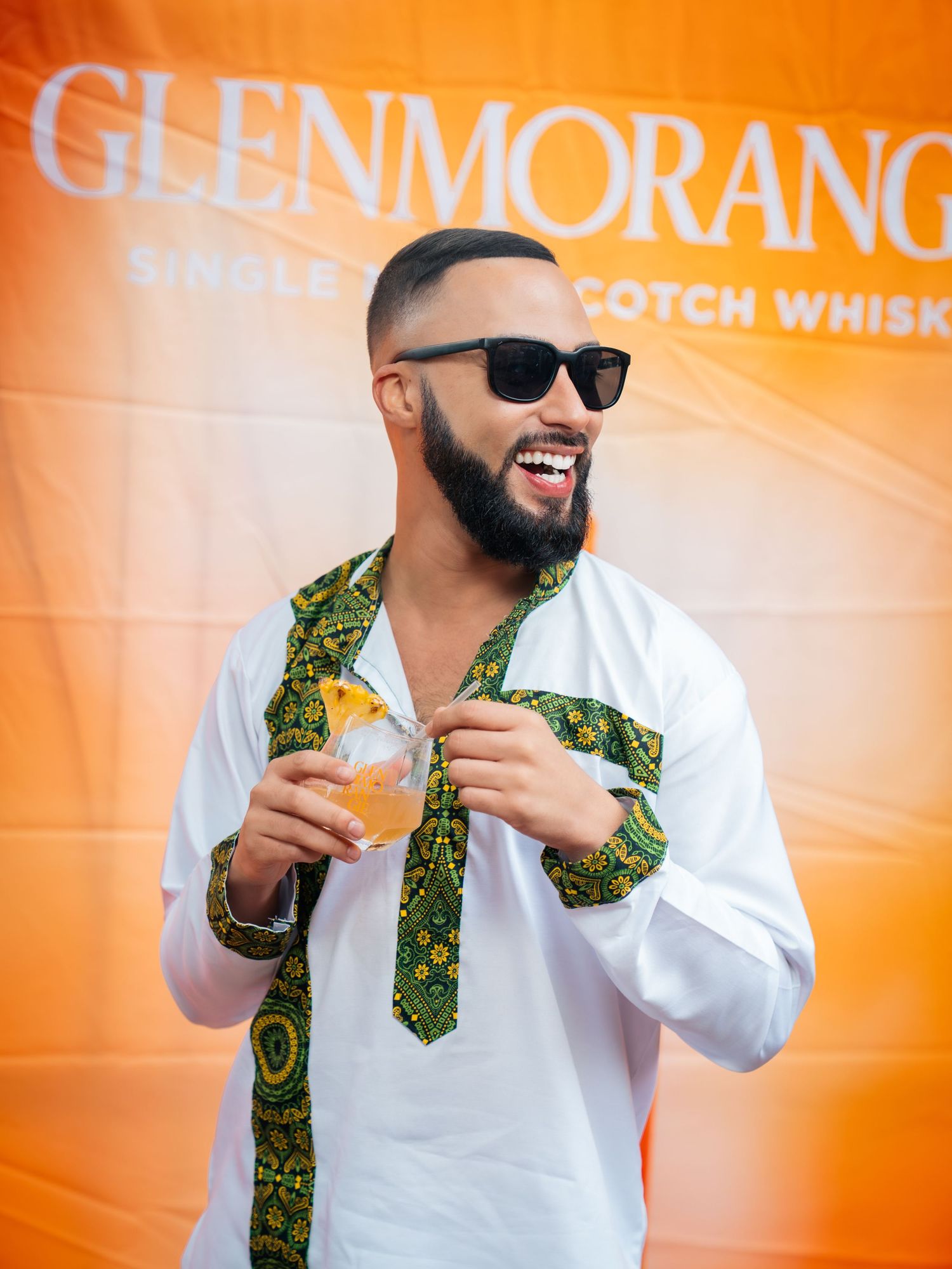 Man smiling in white shirt with green pattern tie, holding cocktail at Glenmorangie Scotch Whisky event.