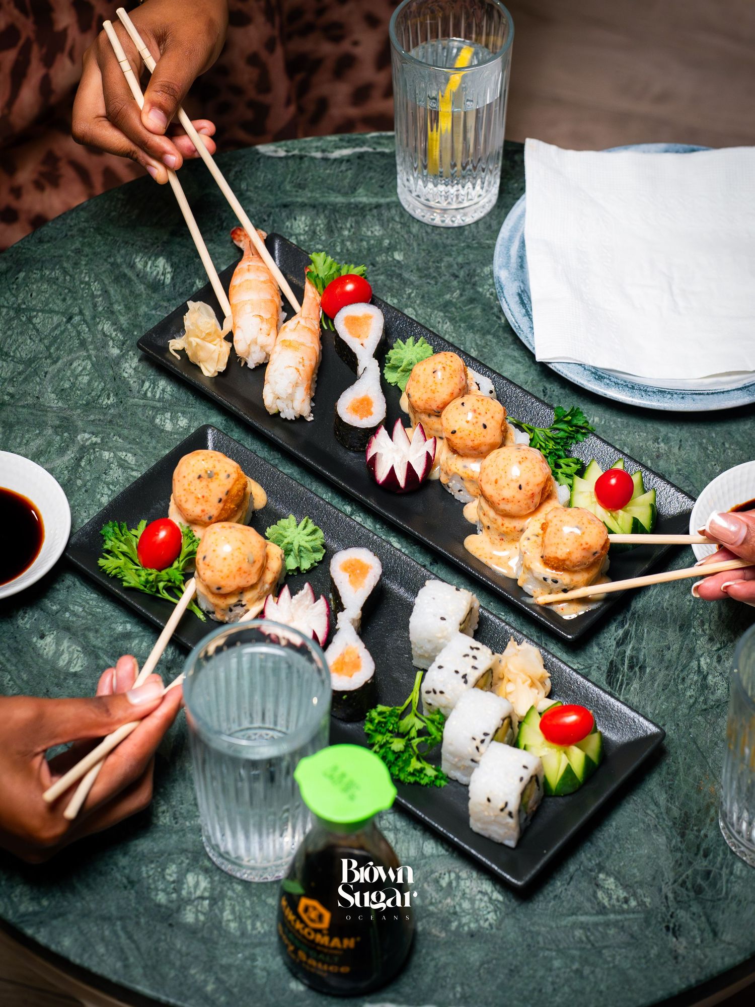 Two people sharing sushi platters with chopsticks on a green marble table at Brown Sugar restaurant.