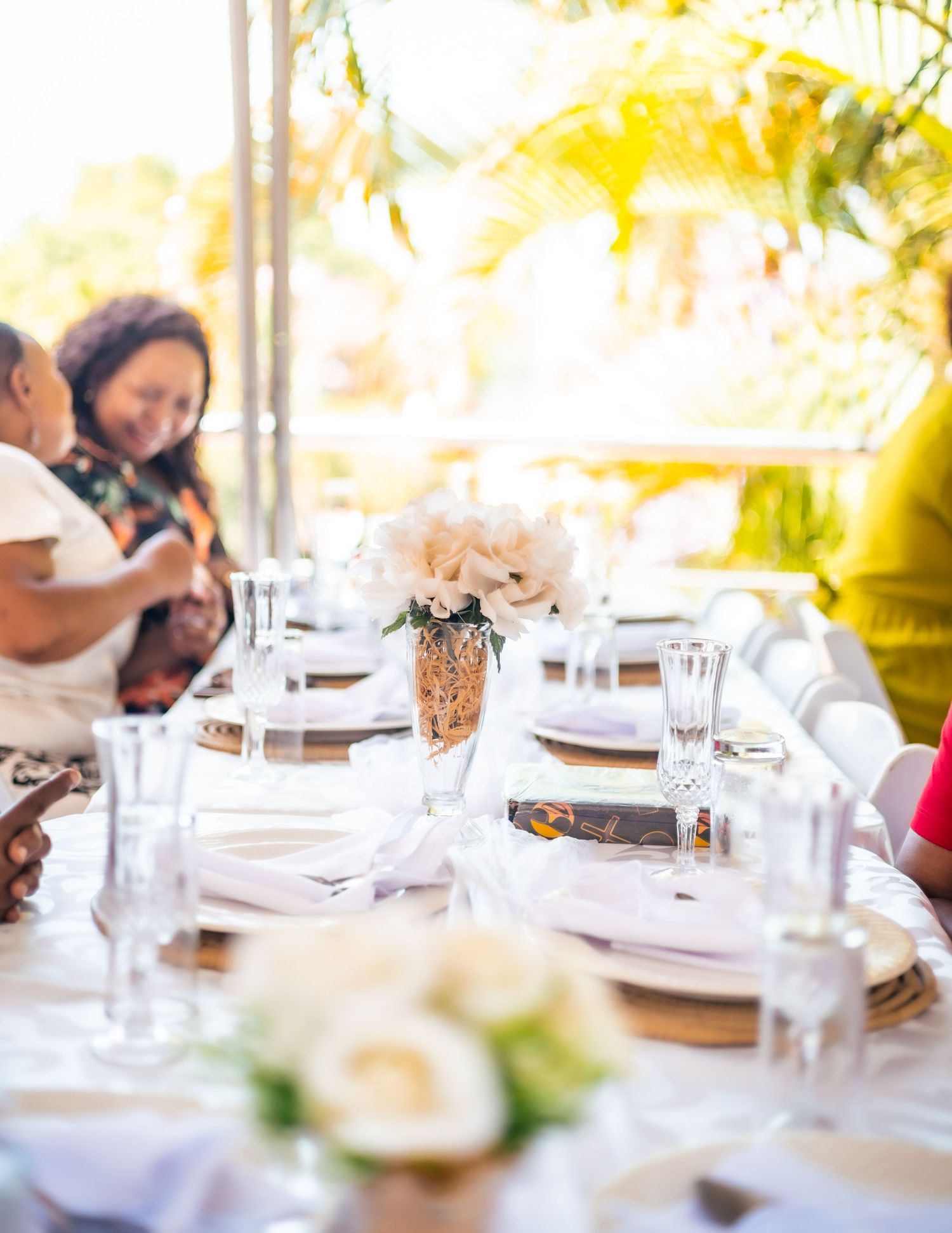 Elegant outdoor wedding reception table set with white floral centerpieces, gold chargers, and glassware under a tent.