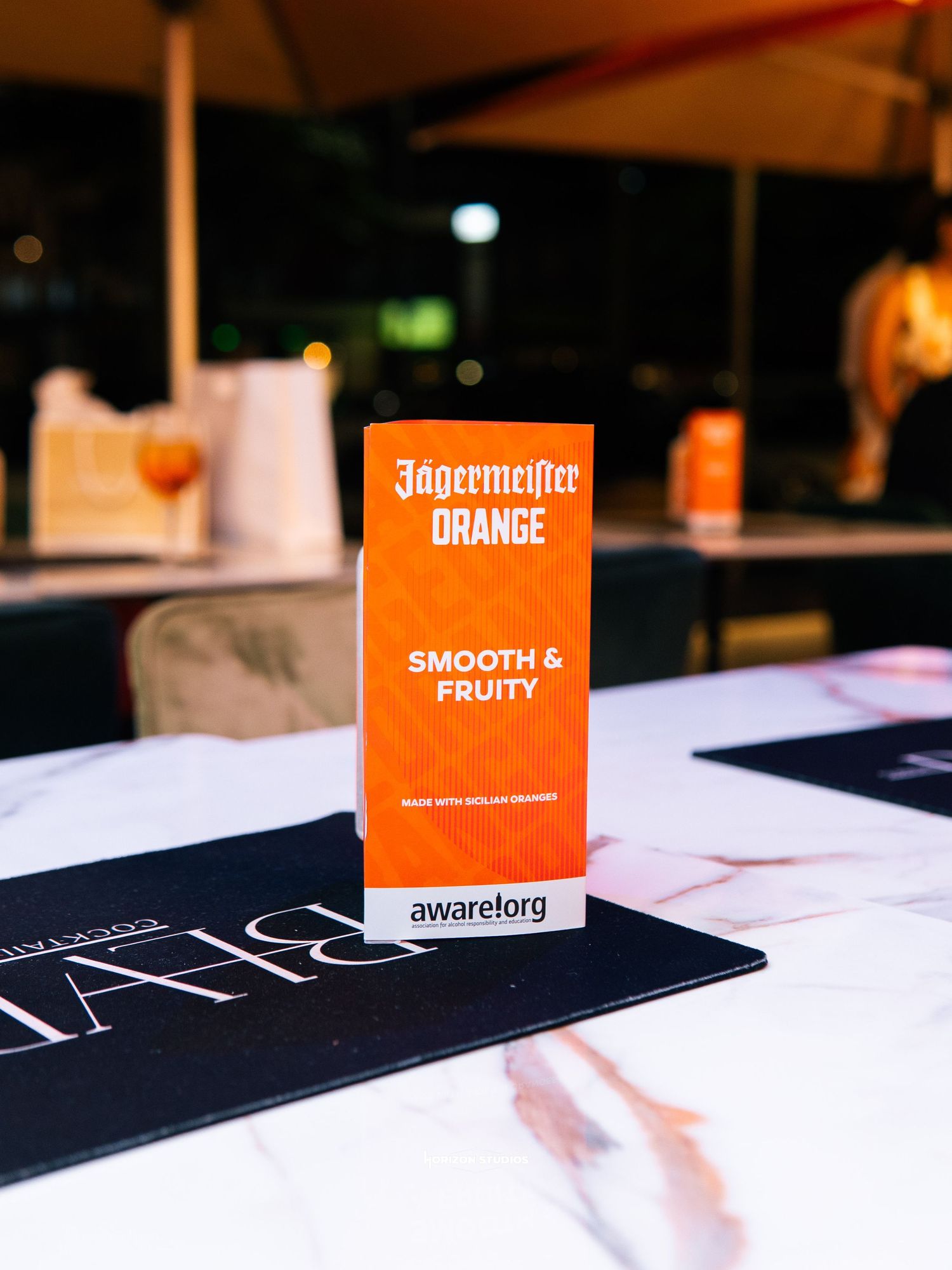 Jägermeister Orange smooth and fruity promotional card displayed on a marble table at an outdoor bar.