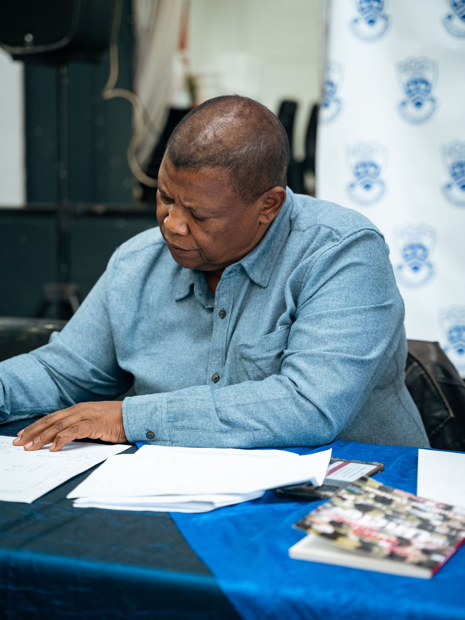 Man in blue shirt reviewing documents at a table with blue tablecloth at a formal signing event.