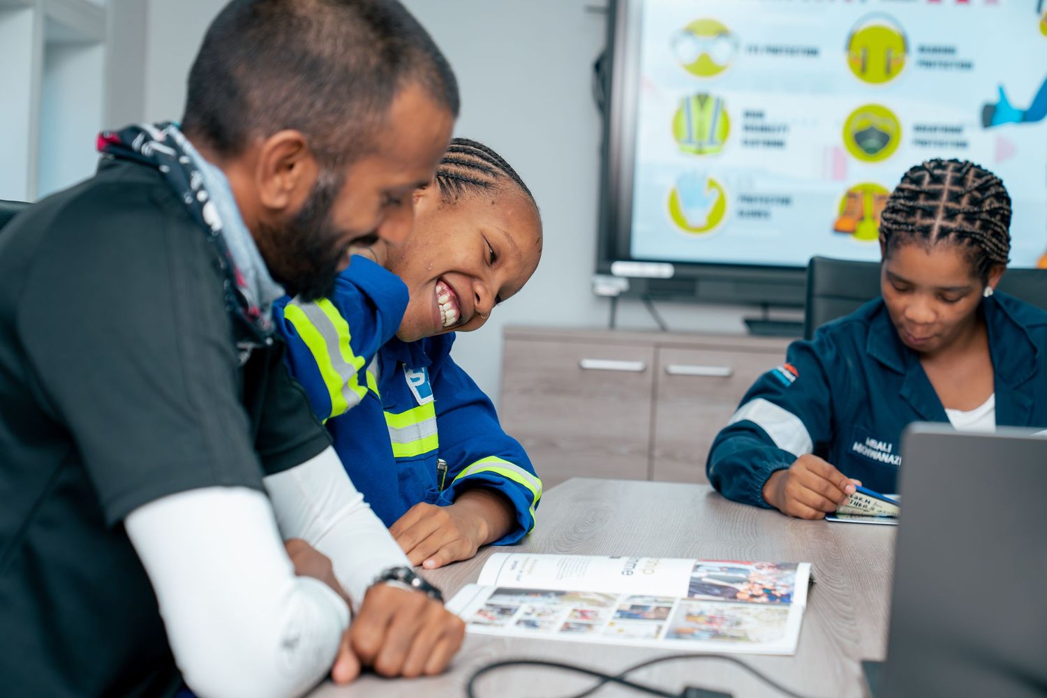 Two professionals in safety vests smile while reviewing documents together in a bright modern conference room.