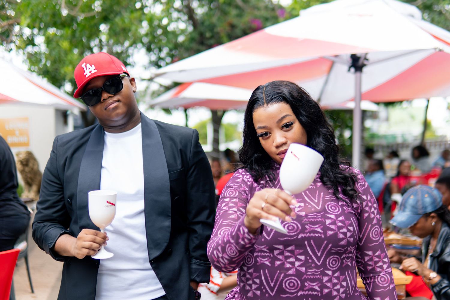 Two people holding white cups at an outdoor event under red and white umbrellas.