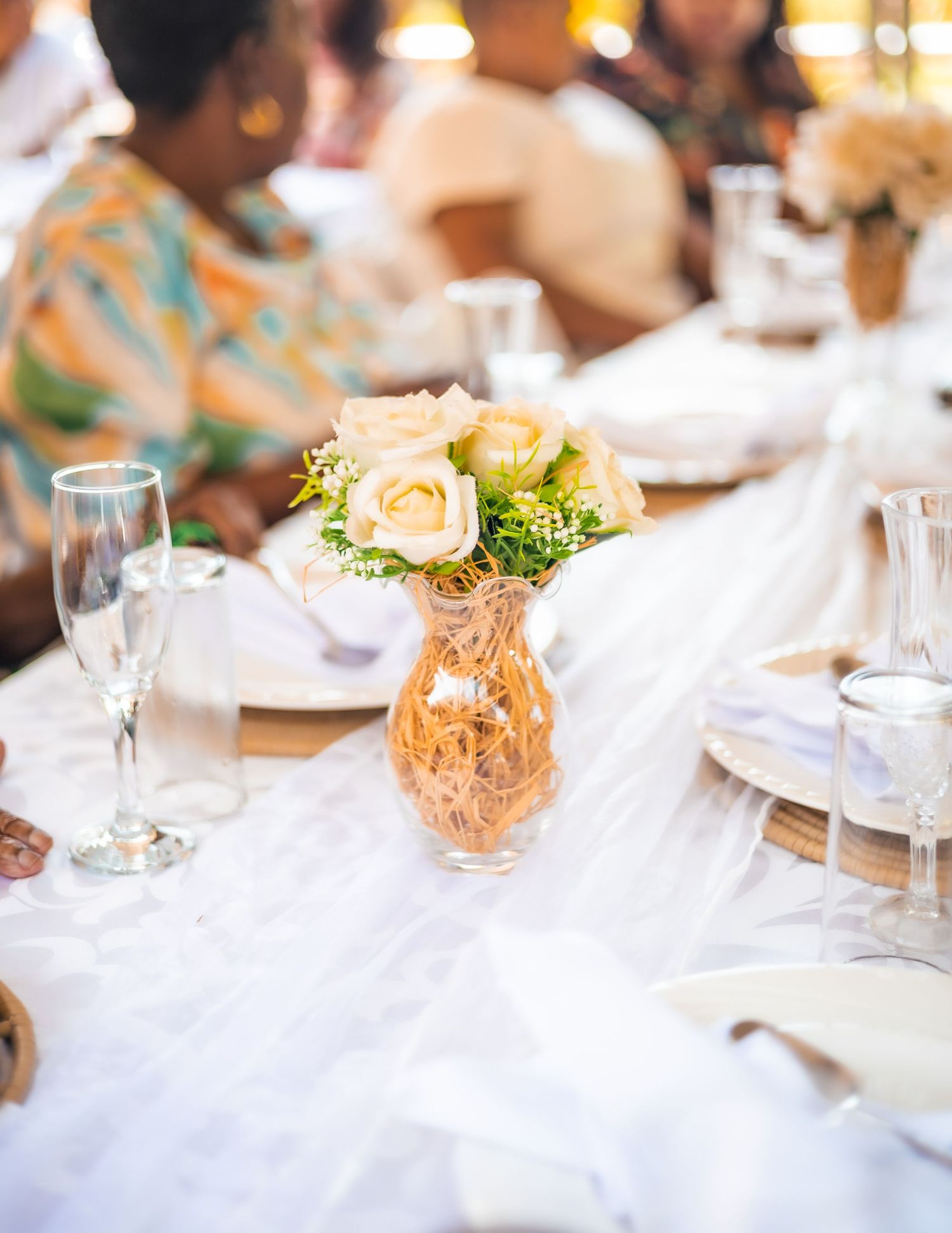 Elegant wedding reception table with white roses in a gold vase, champagne flutes, and white linen decor.