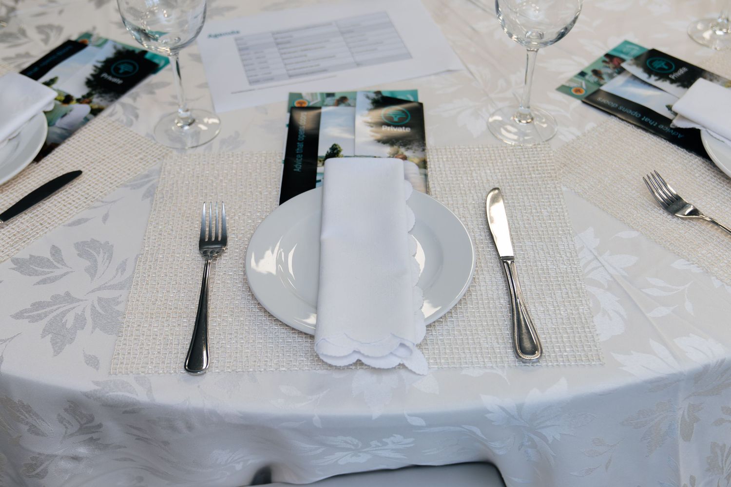 Elegant wedding table setting with white damask tablecloth, folded napkin on plate, silverware, and crystal glasses.